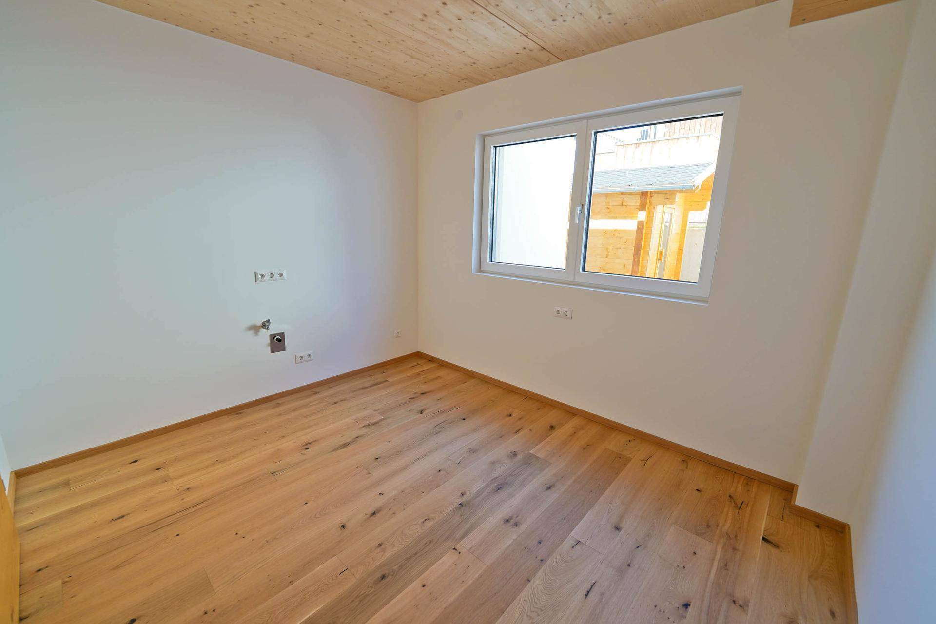 Helles Zimmer mit Holzboden und Fenster, bereit zur individuellen Gestaltung.