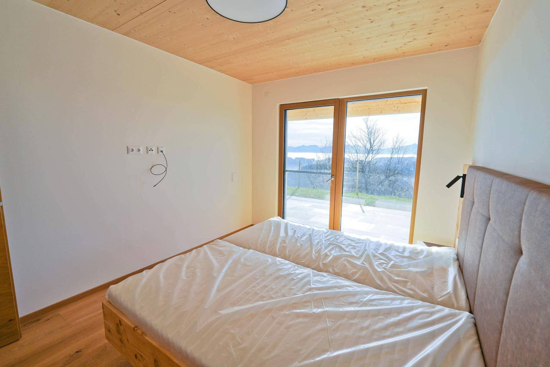 Helles Schlafzimmer mit Holzboden, Doppelbett und Terrassenzugang mit Weitblick.