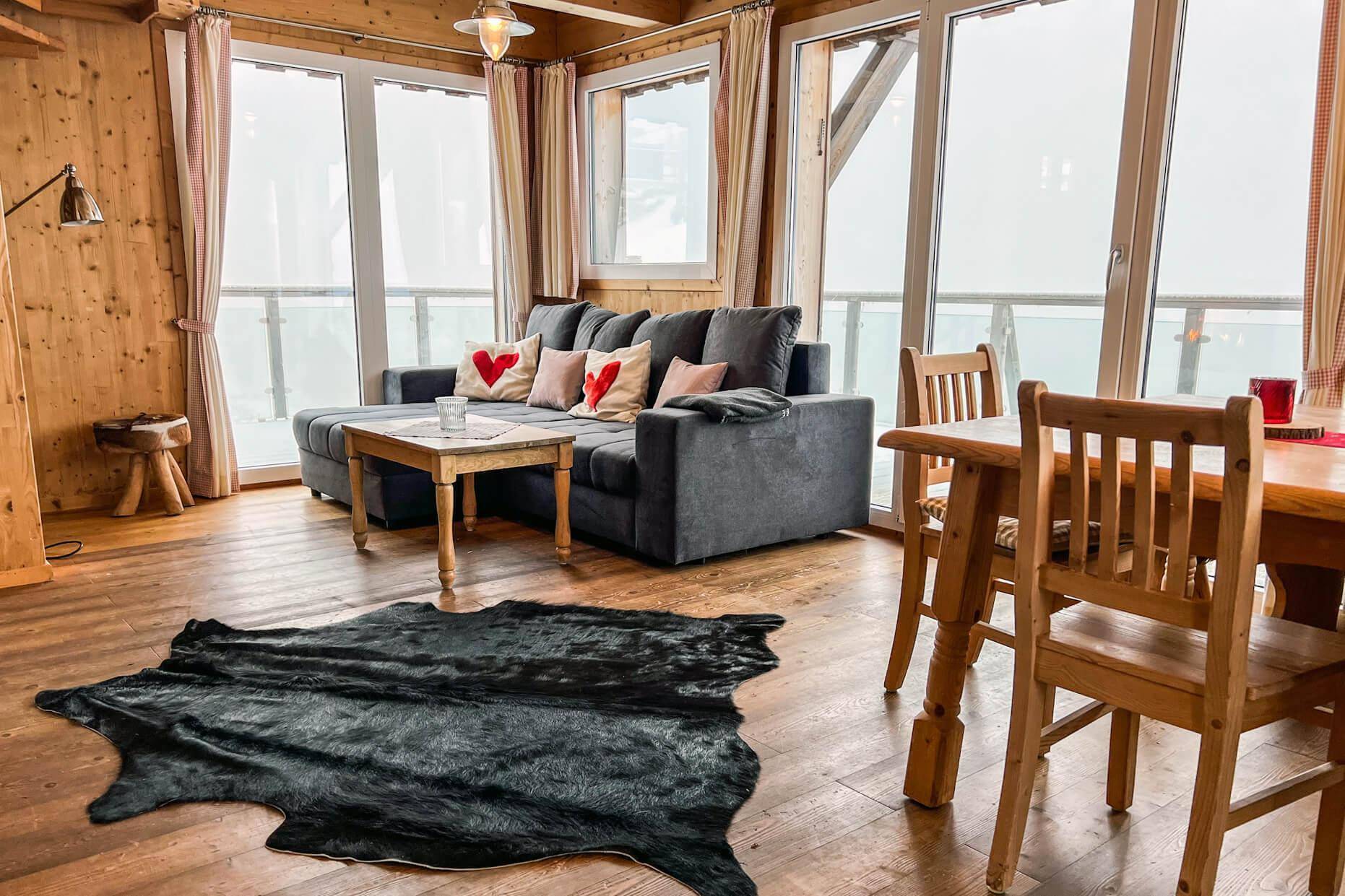 Heller Wohnbereich mit bequemer Couch, Holzboden und großen Fenstern mit Panoramablick.