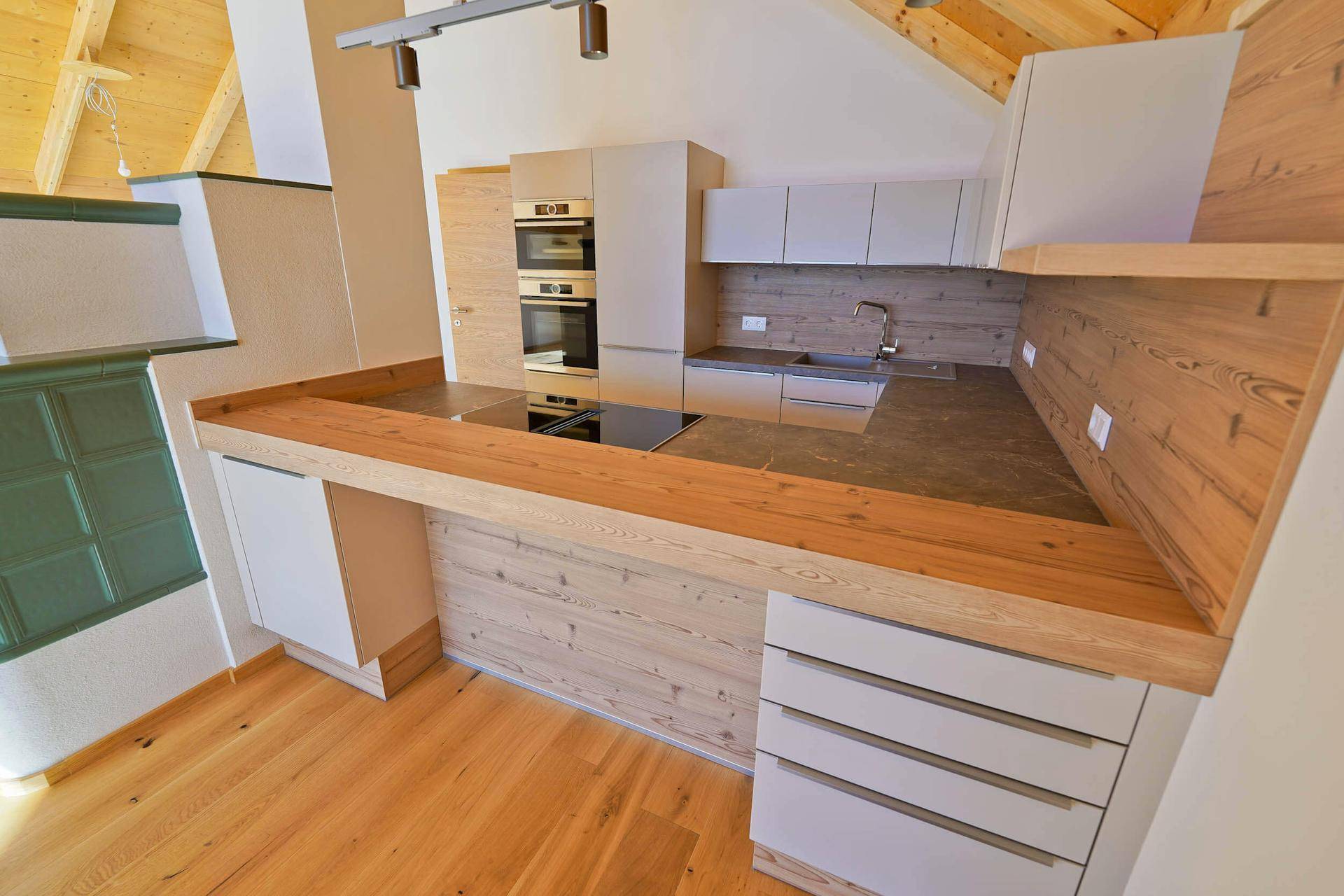 Moderne Einbauküche mit Holztheke, Induktionskochfeld und hellen Schränken unter der Dachschräge.