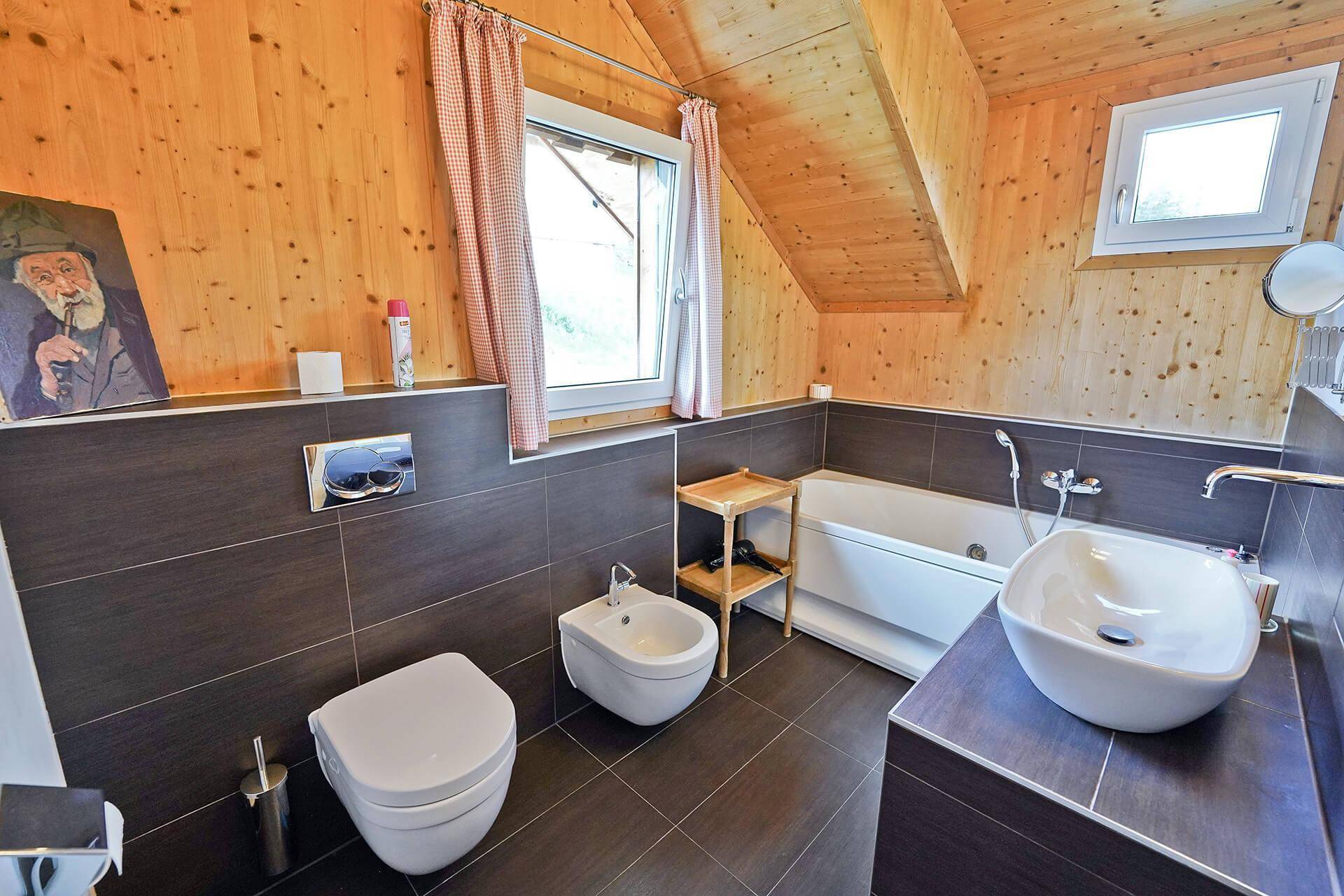 Modernes Badezimmer mit Badewanne, Bidet, wandhängendem WC und dunklen Fliesen.