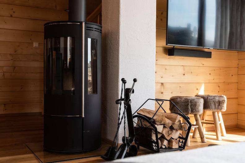 Detailansicht des Kaminofens mit Holzscheiten und Kaminbesteck im Wohnzimmer.