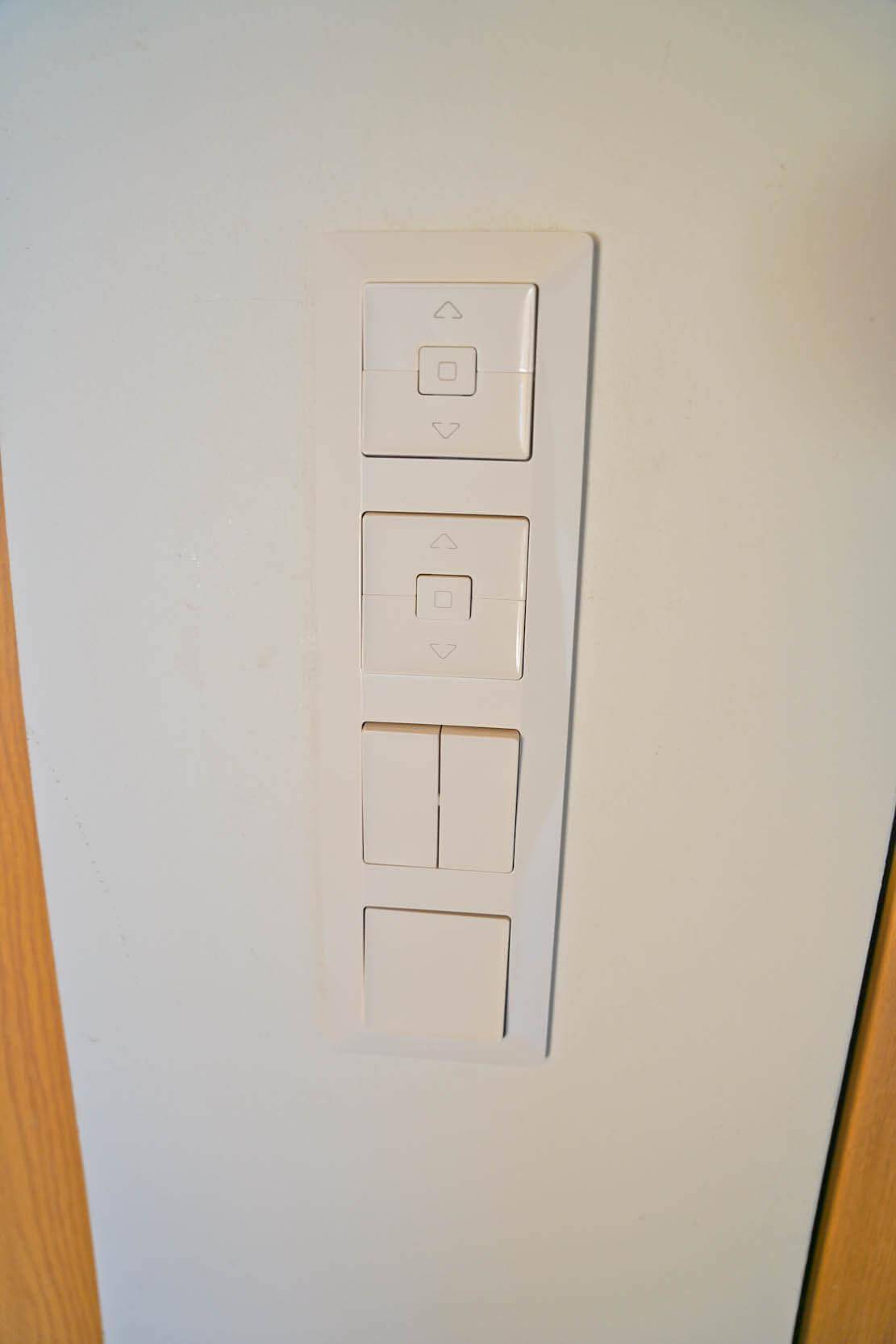 Modernes Bedienfeld für Licht und Jalousien an einer weißen Wand.
