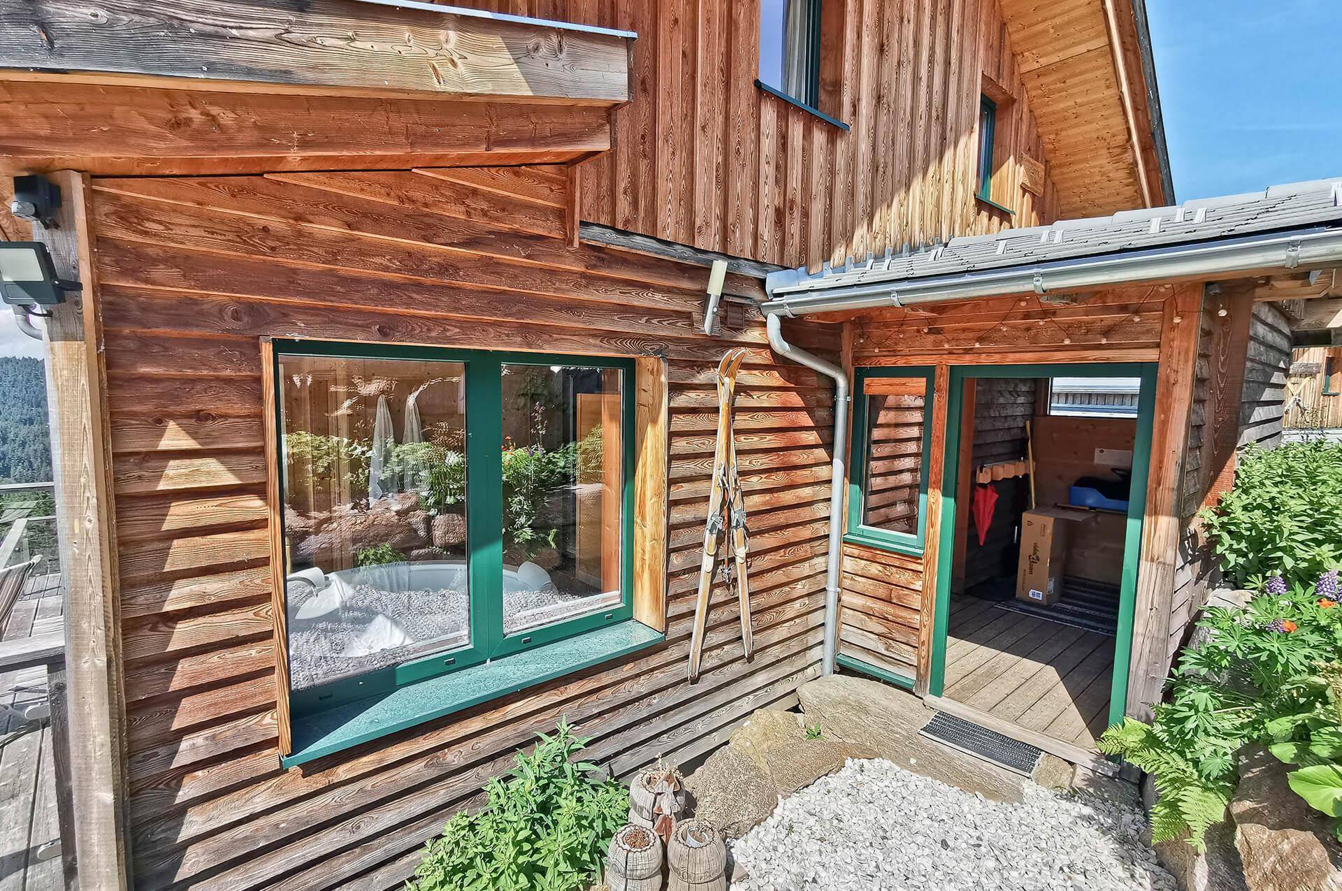 Eingangsbereich des Holzchalets mit grünen Fensterrahmen und einem kleinen Kiesweg.