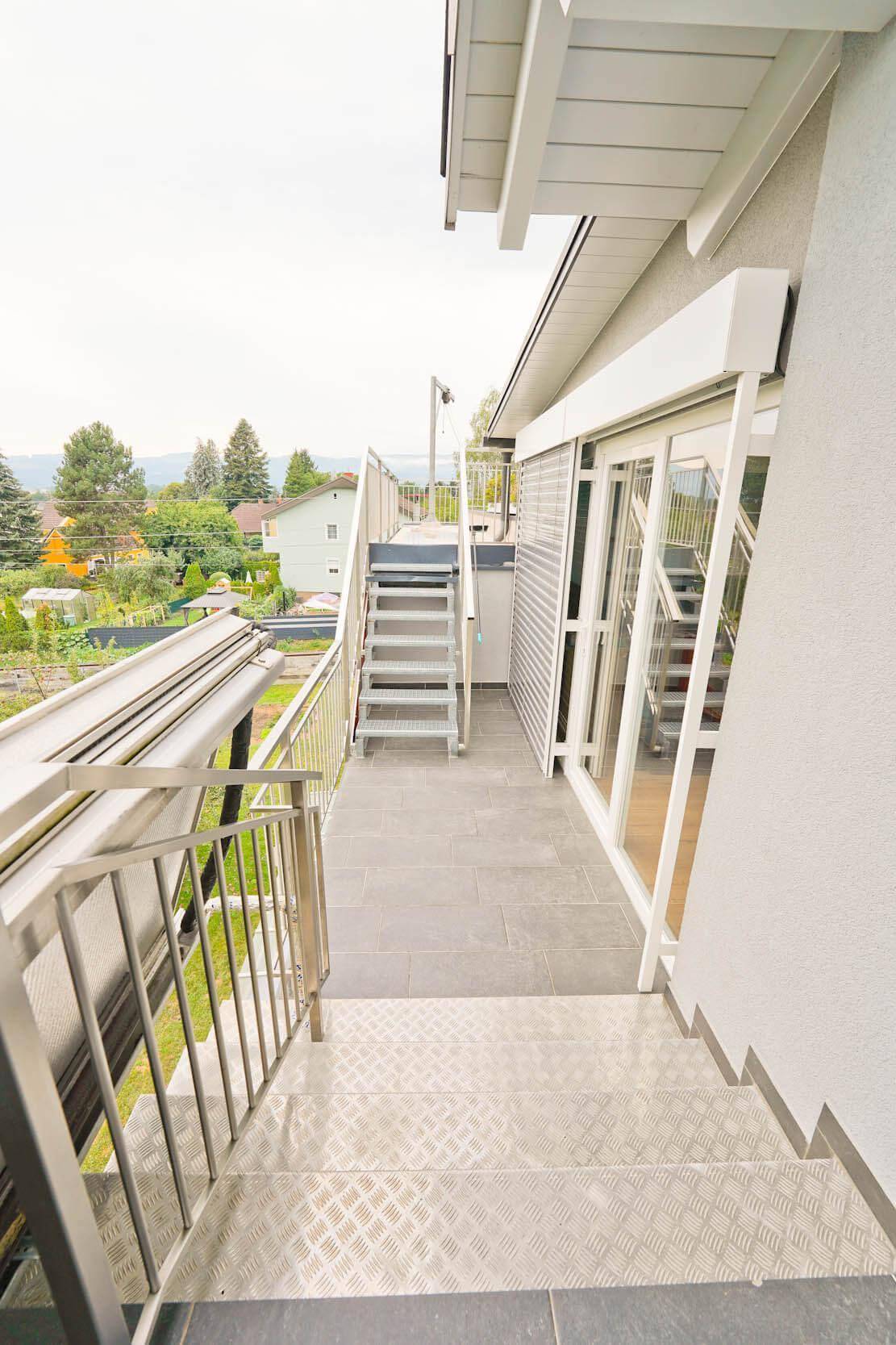 Balkon mit Treppe, die zu einer oberen Ebene oder Dachterrasse führt, mit Blick ins Grüne.