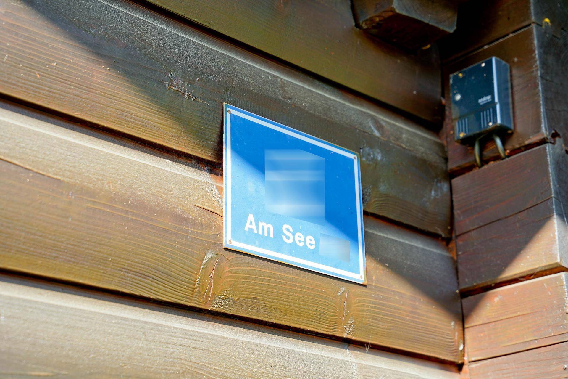 Blaues Schild mit der Aufschrift "Am See" an der Holzfassade des Gebäudes.