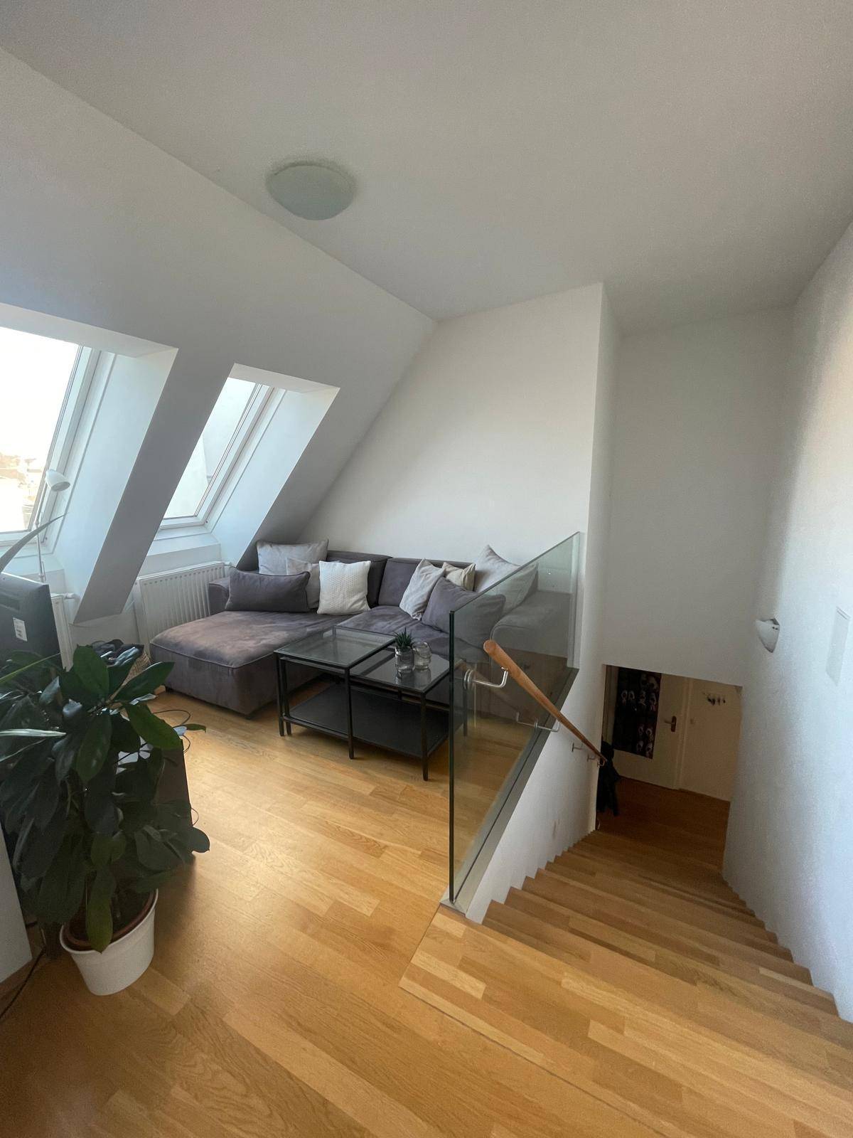 Wohnzimmer mit Dachschrägen, Holzboden und einer modernen Treppe mit Glasgeländer.