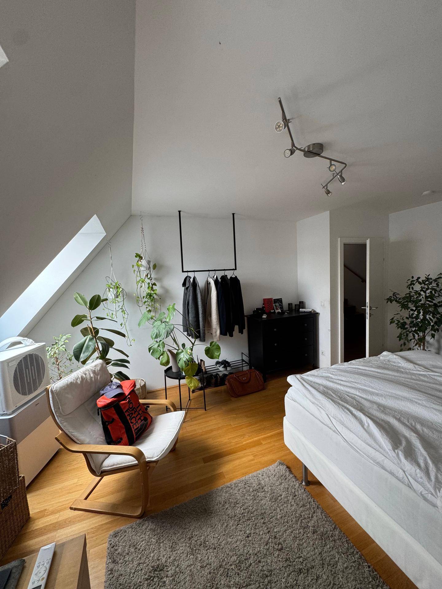 Gemütliches Schlafzimmer mit Holzboden, Pflanzen und einer offenen Kleiderstange unter der Dachschräge.