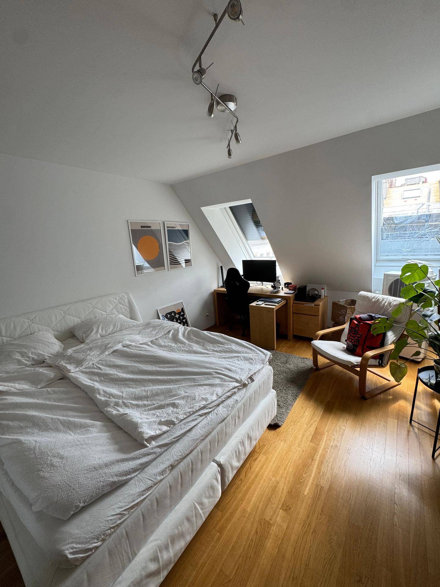 Schlafzimmer mit Dachschrägen, Holzboden und einem Arbeitsbereich unter dem Dachfenster.