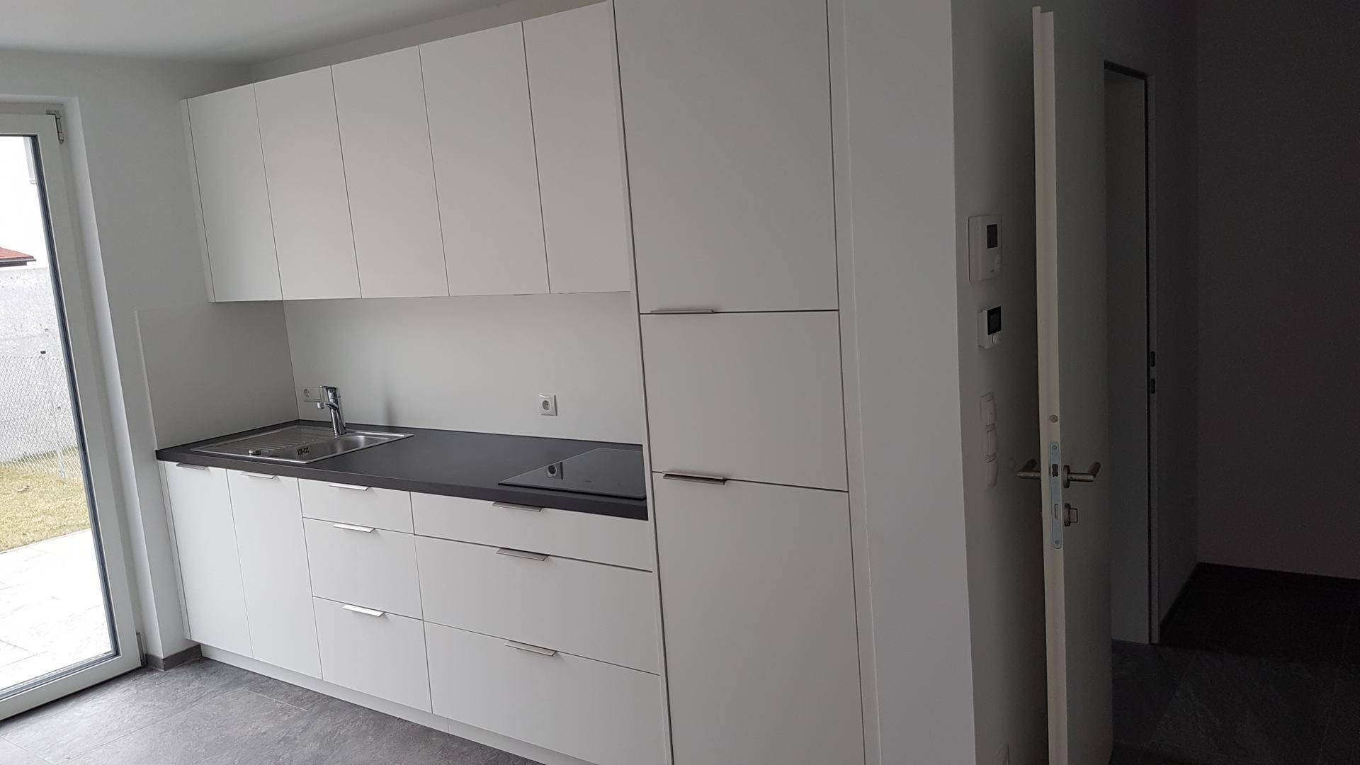 Moderne, weiße Einbauküche mit integrierten Geräten und Zugang zu einem Außenbereich.