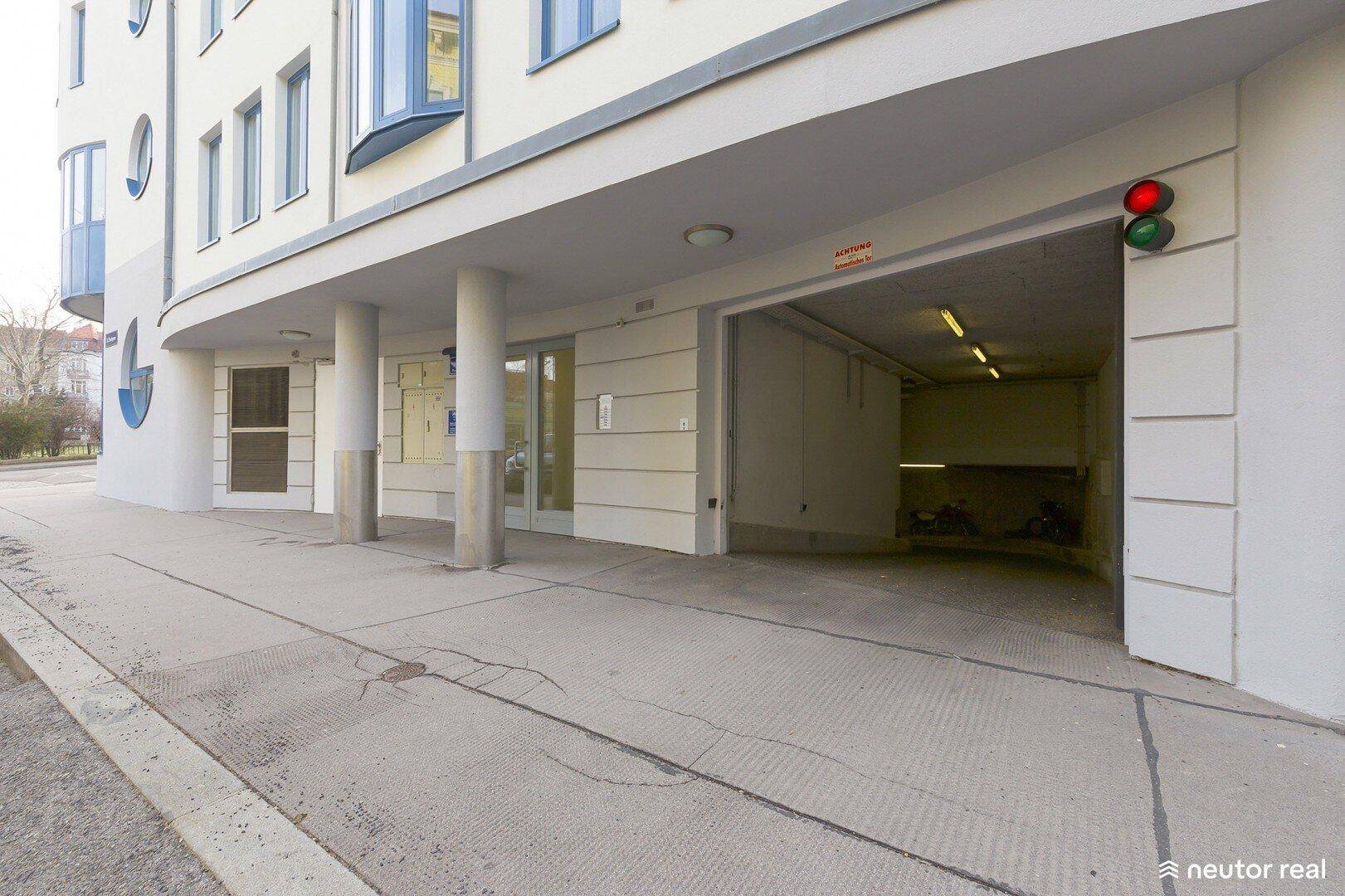 Einfahrt zur Tiefgarage eines modernen Wohngebäudes mit Ampelsystem und Säulen.