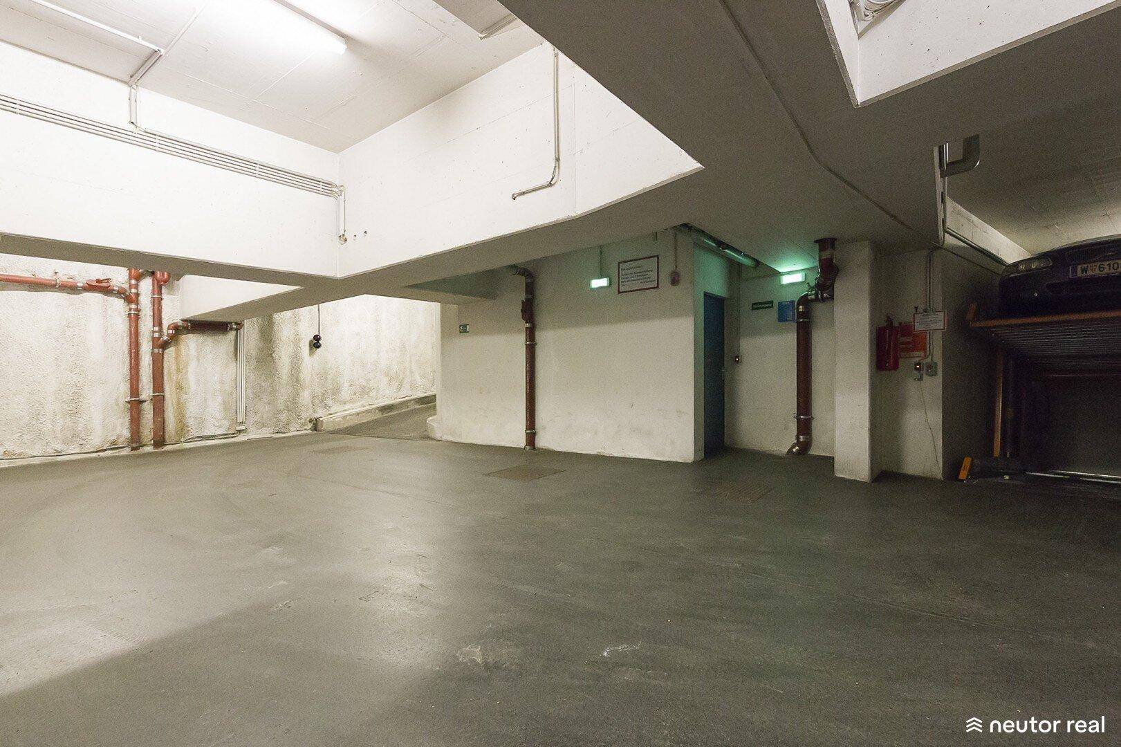 Weitere Ansicht der Tiefgarage mit Betonwänden, sichtbaren Rohren und Brandschutzvorrichtungen.