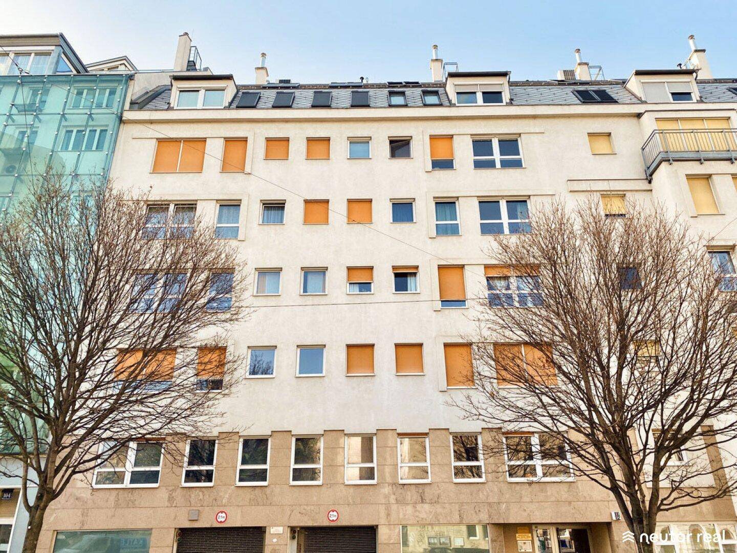 Fassade eines Mehrfamilienhauses mit vielen Fenstern und orangefarbenen Rollläden.
