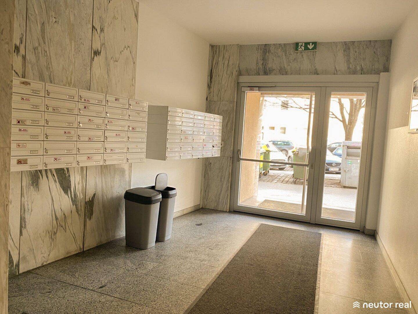 Eingangsbereich des Gebäudes mit Marmorwänden, Briefkästen und Glastür zur Straße.