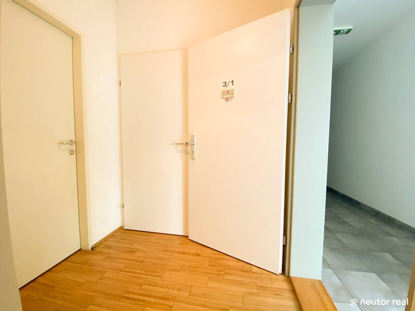 Heller Flur mit Holzboden und zwei weißen Türen, eine davon offen.