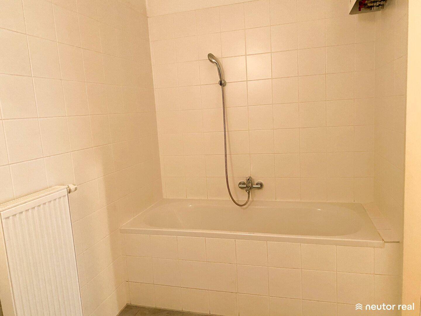 Badewanne mit Duscharmatur und gefliesten Wänden, inklusive Heizkörper.