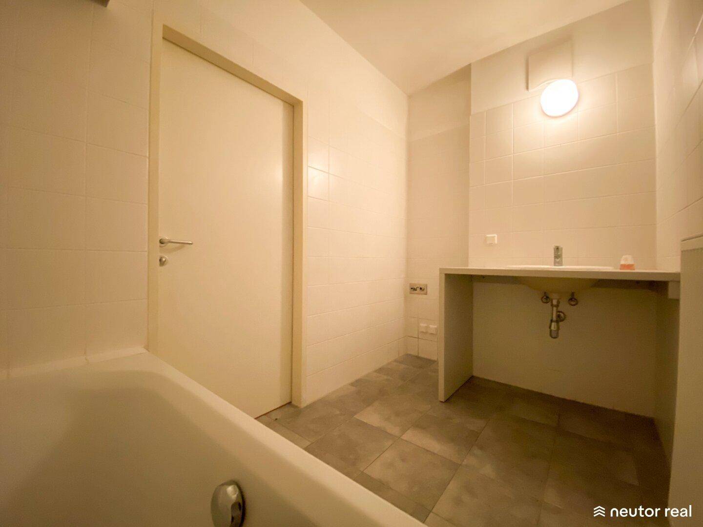 Badezimmer mit Badewanne und gefliesten Wänden, bereit für die Installation des Waschtischs.