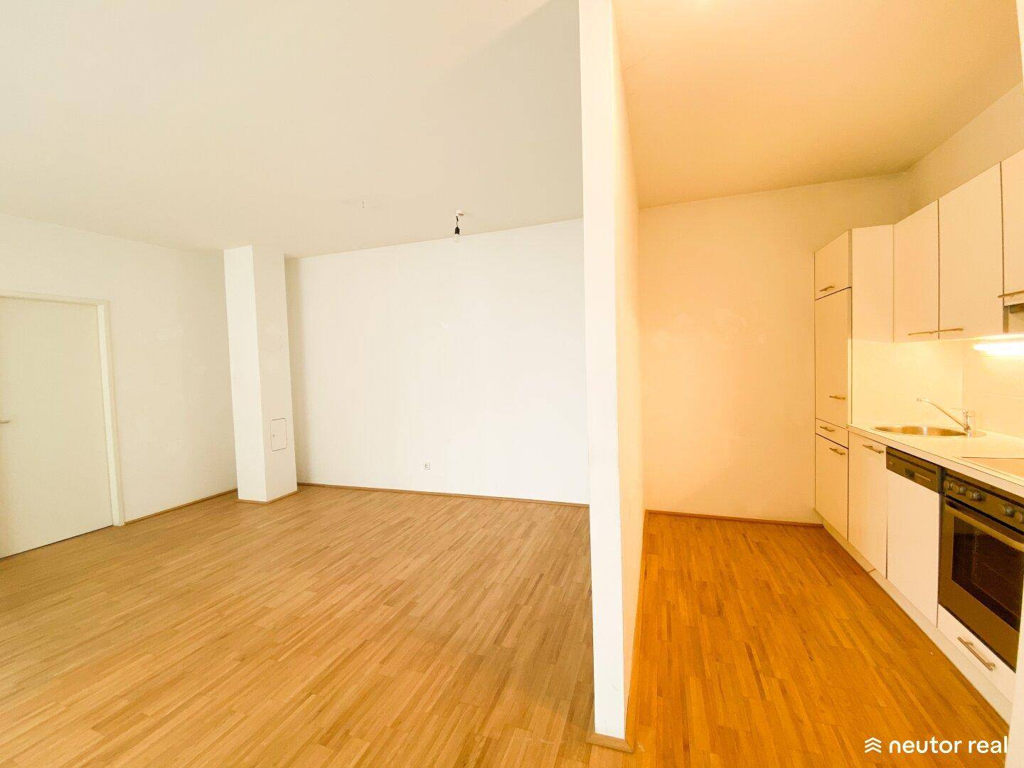 Offener Wohnbereich mit Holzboden und angrenzender, kleiner Einbauküche.