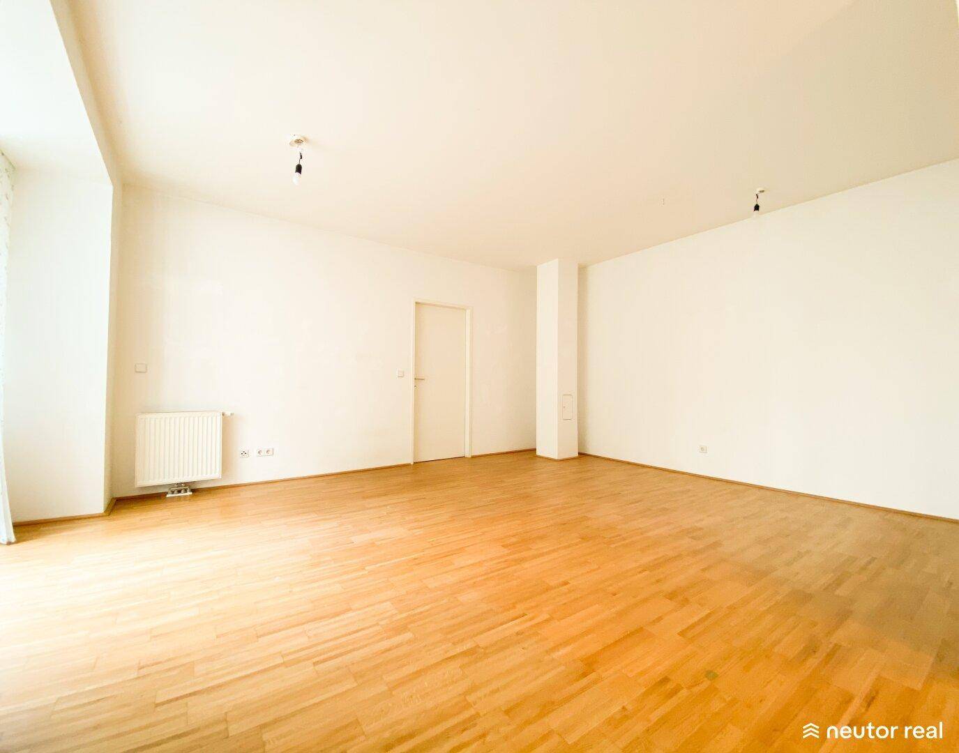 Geräumiges, leeres Wohnzimmer mit hellem Holzboden und weißen Wänden.