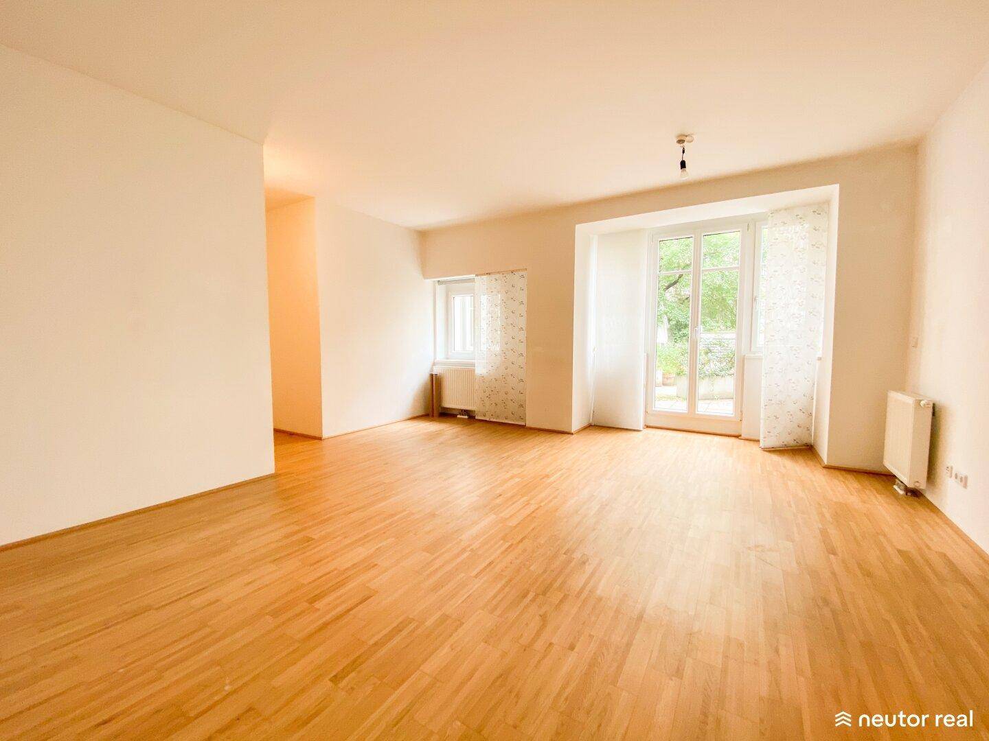 Helles Wohnzimmer mit Holzboden und großen Fenstern, die Zugang nach draußen bieten.