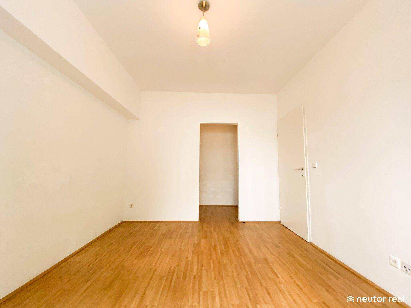Leeres Zimmer mit Holzboden und weißen Wänden, ideal als Schlaf- oder Arbeitszimmer.
