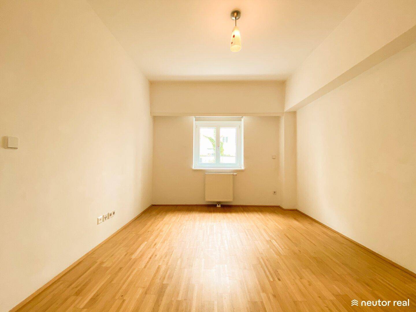 Helles Schlafzimmer mit Holzboden, weißen Wänden und einem Fenster.