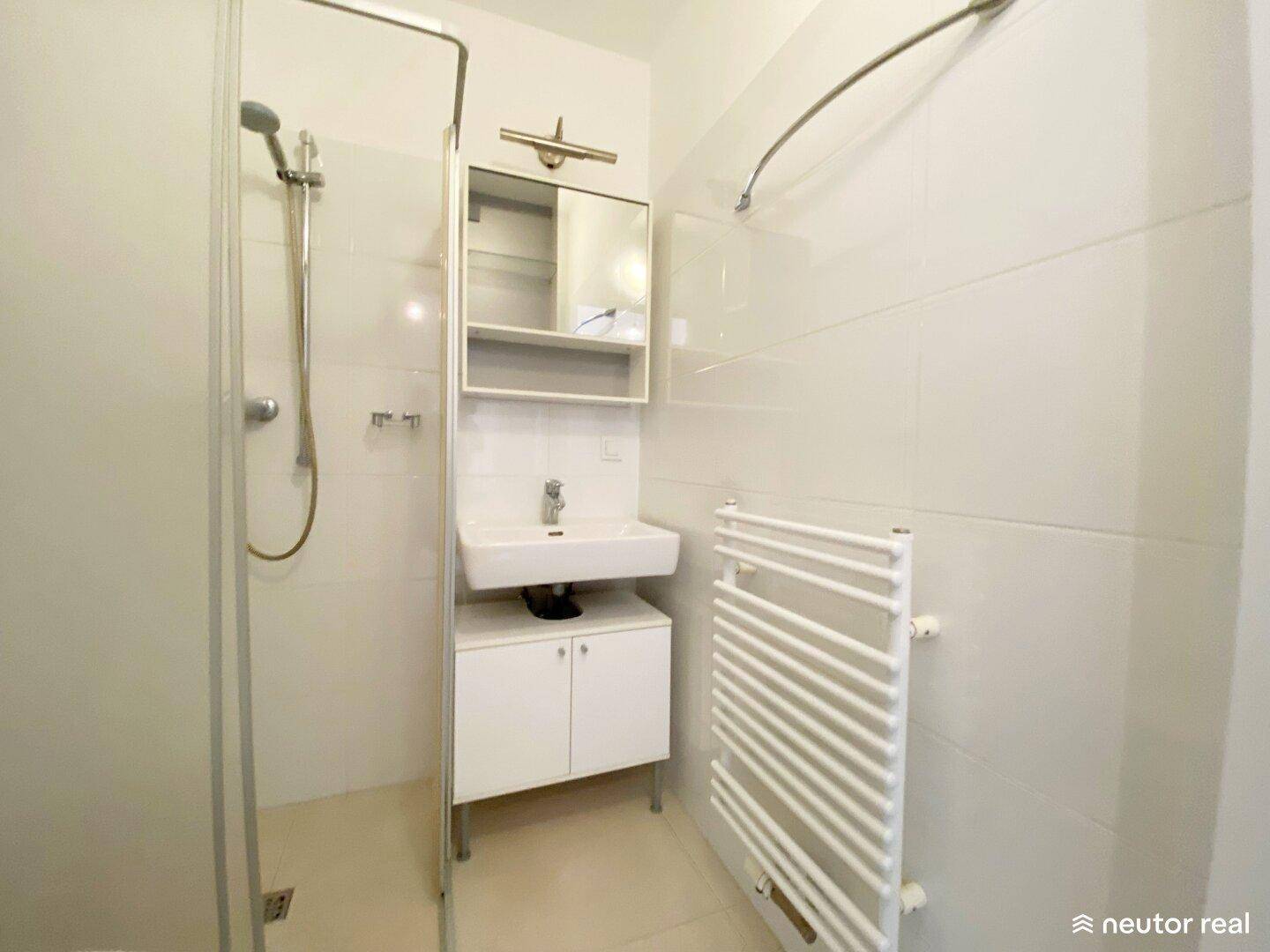 Modernes Badezimmer mit Duschkabine, Waschbecken und beheiztem Handtuchhalter in hellen Fliesen.
