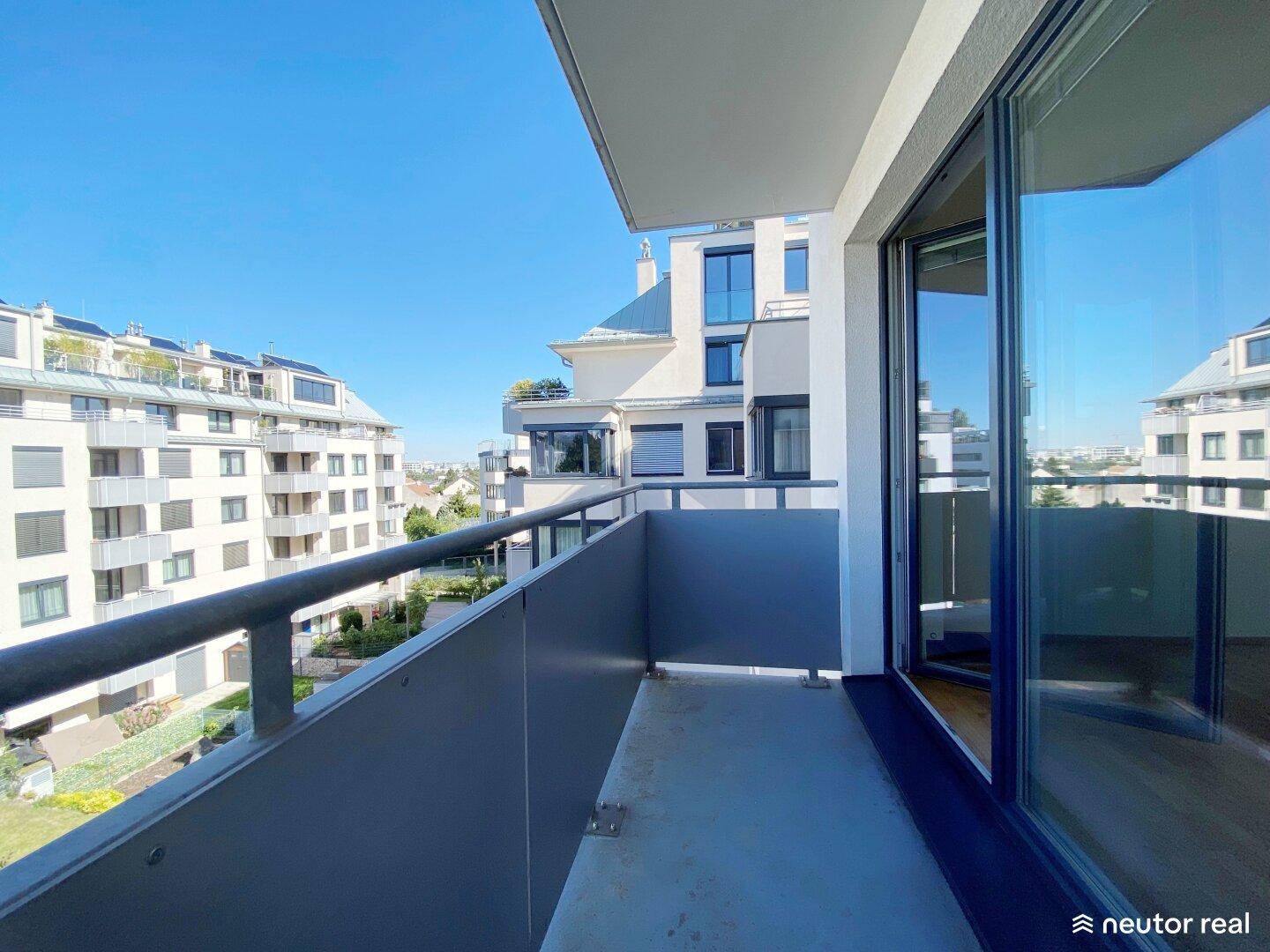 Geräumiger Balkon mit Blick auf moderne Wohngebäude und grüne Umgebung unter blauem Himmel.