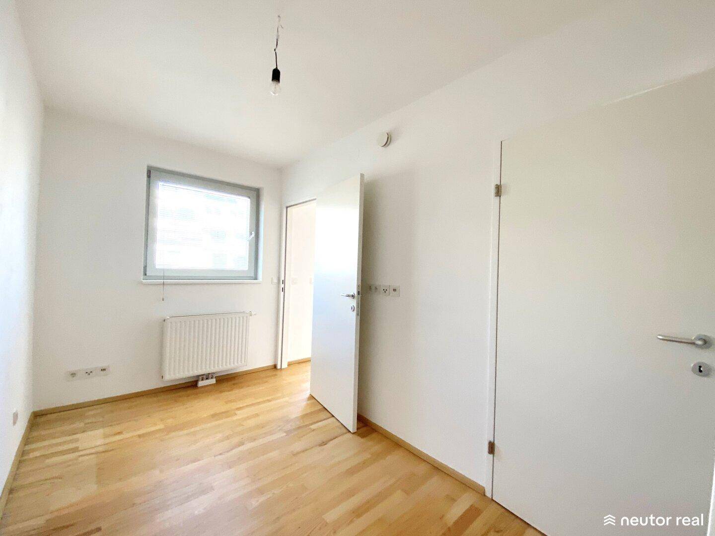 Helles Schlafzimmer mit Parkettboden, Fenster und Heizkörper, bereit zur Einrichtung.