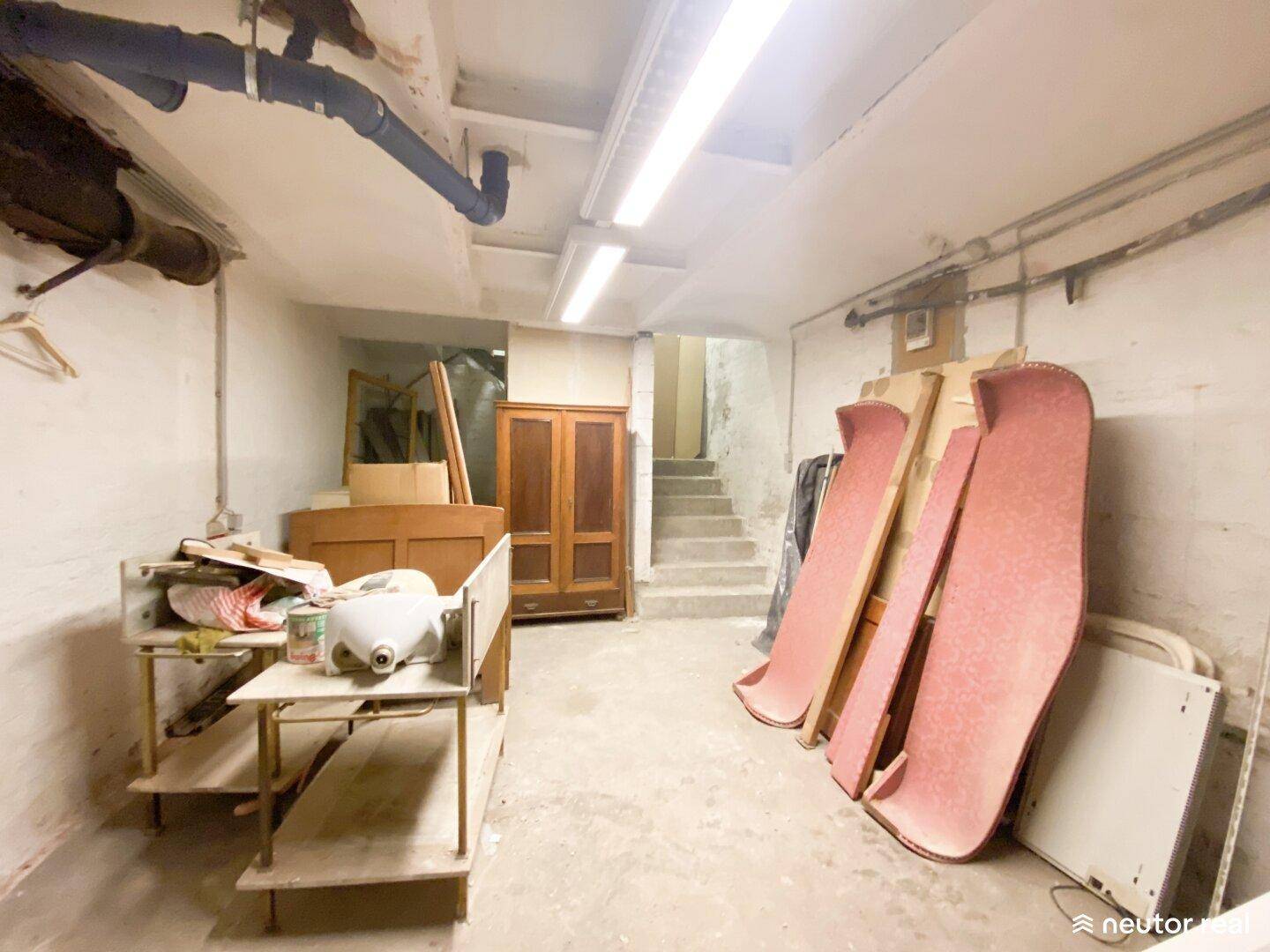 Geräumiger Kellerraum mit Treppenzugang, verschiedenen Möbeln und Baumaterialien, in Renovierungszustand.