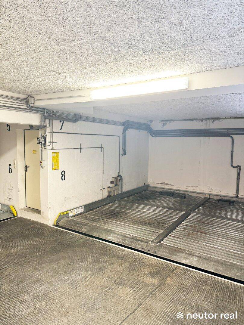 Heller Tiefgaragenstellplatz mit Doppelparker-System und funktionalen Installationen an der Decke.