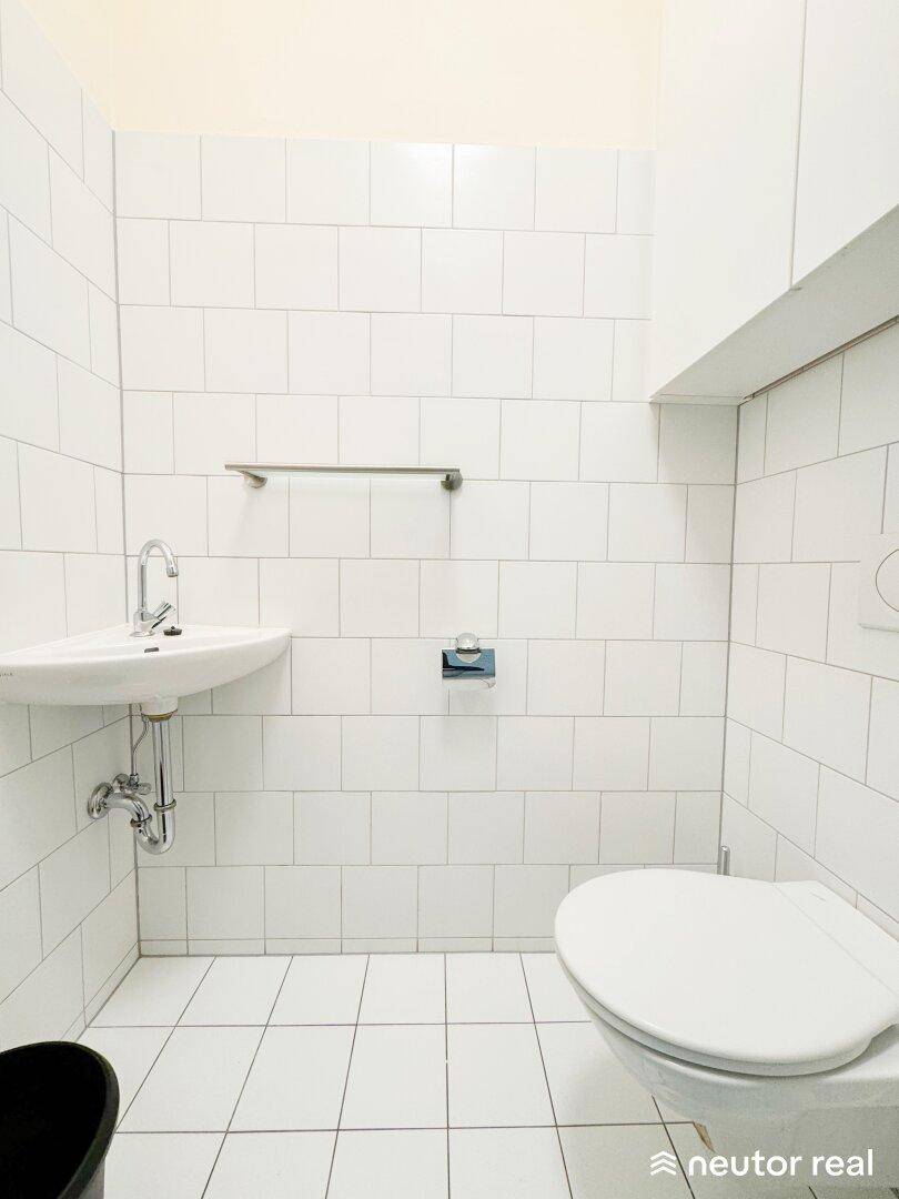 Einfache Gästetoilette mit weiß gefliesten Wänden, Waschbecken und WC.