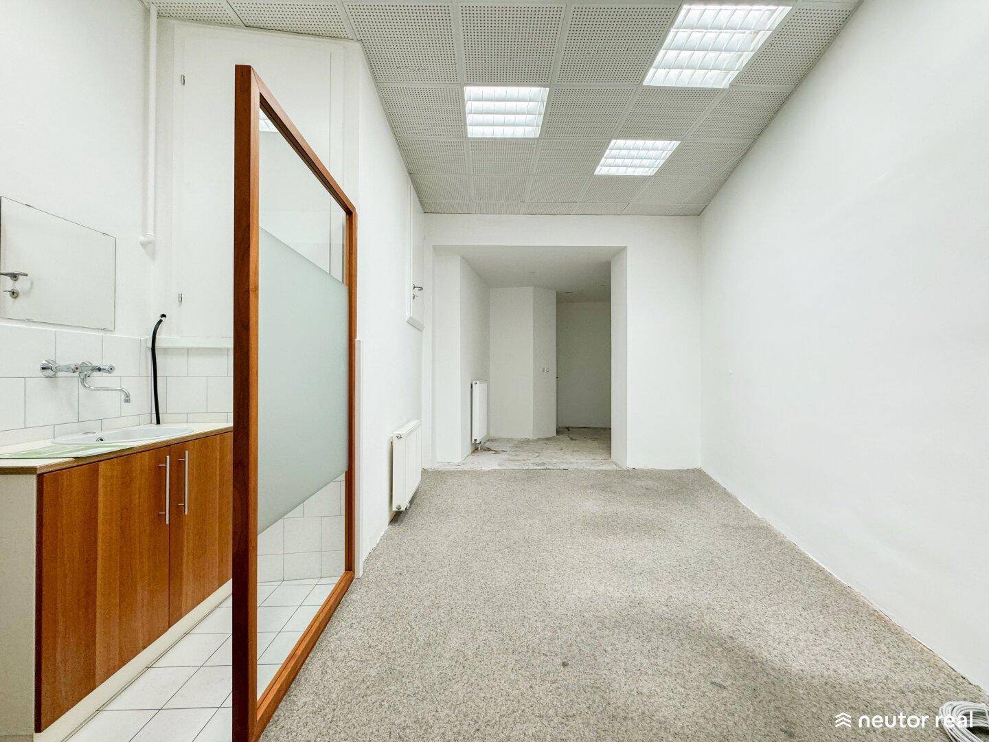 Langer Geschäftsraum mit Teppichboden, einer Theke mit Waschbecken und einem Milchglas-Raumteiler.