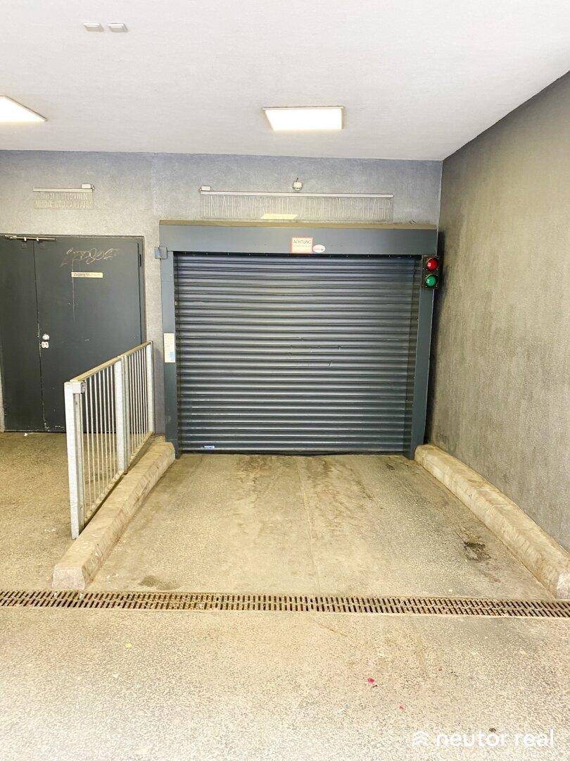 Eingangsbereich einer Tiefgarage mit geschlossenem Rolltor und einem Ampelsystem zur Verkehrsregelung.