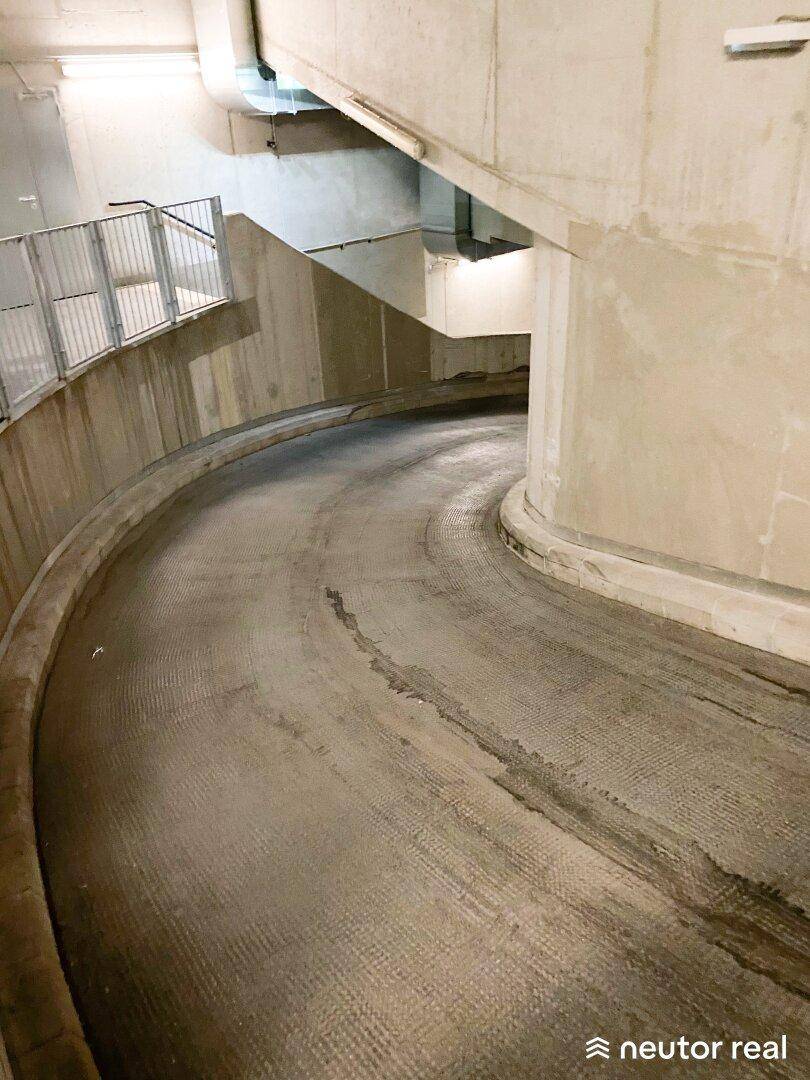 Geschwungene Auffahrtsrampe in einer Tiefgarage mit Betonwänden und einem stabilen Metallgeländer.