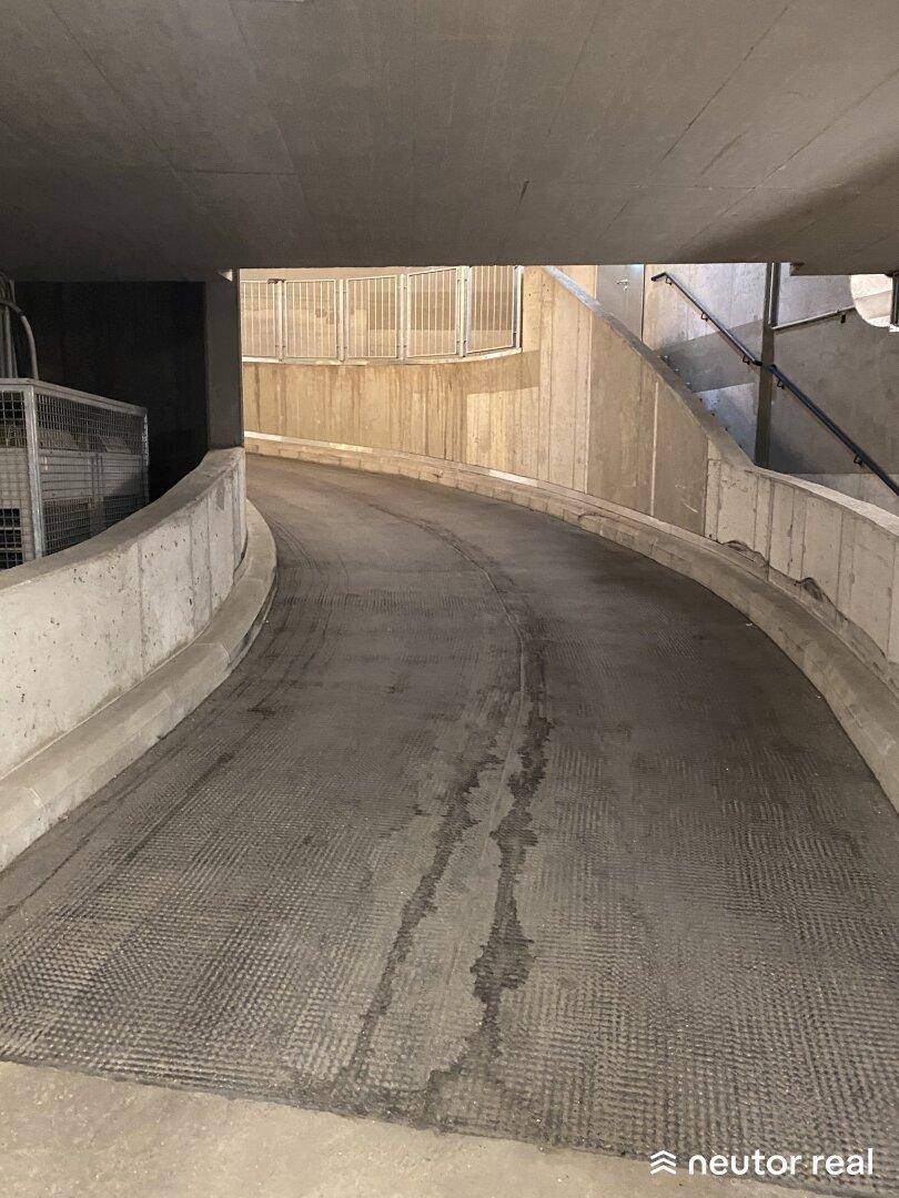 Breite, geschwungene Rampe in einer Tiefgarage, umgeben von robusten Betonstrukturen und einem Geländer.