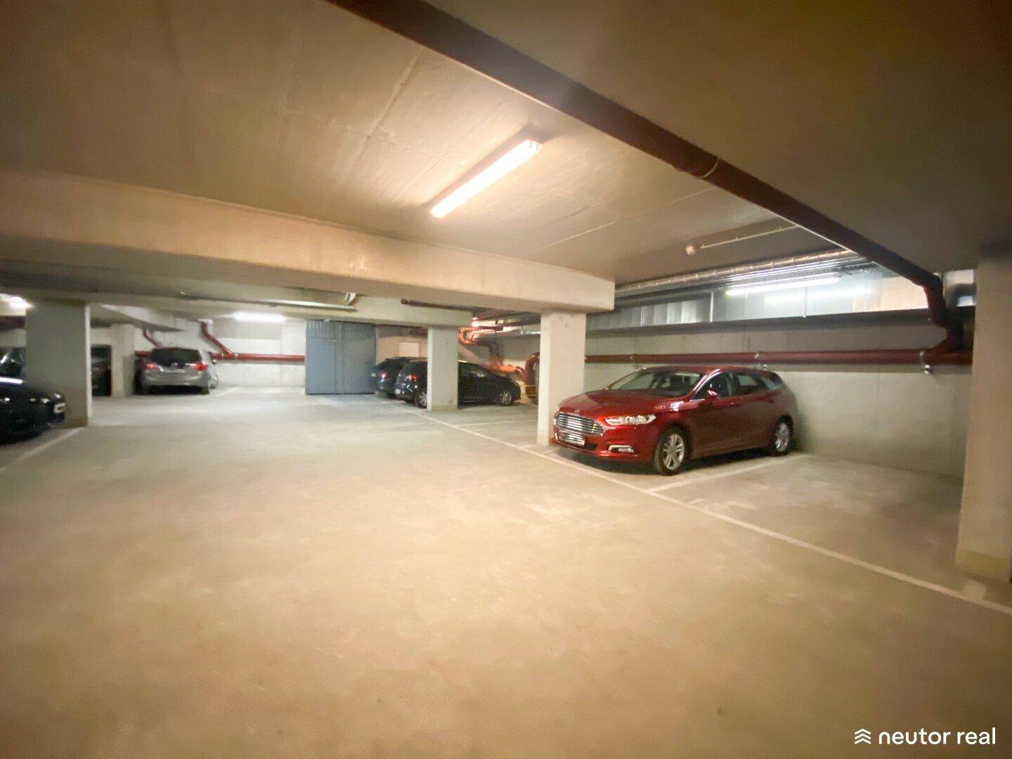 Helle Tiefgarage mit Betonboden und Deckenleuchten, in der mehrere Autos abgestellt sind.