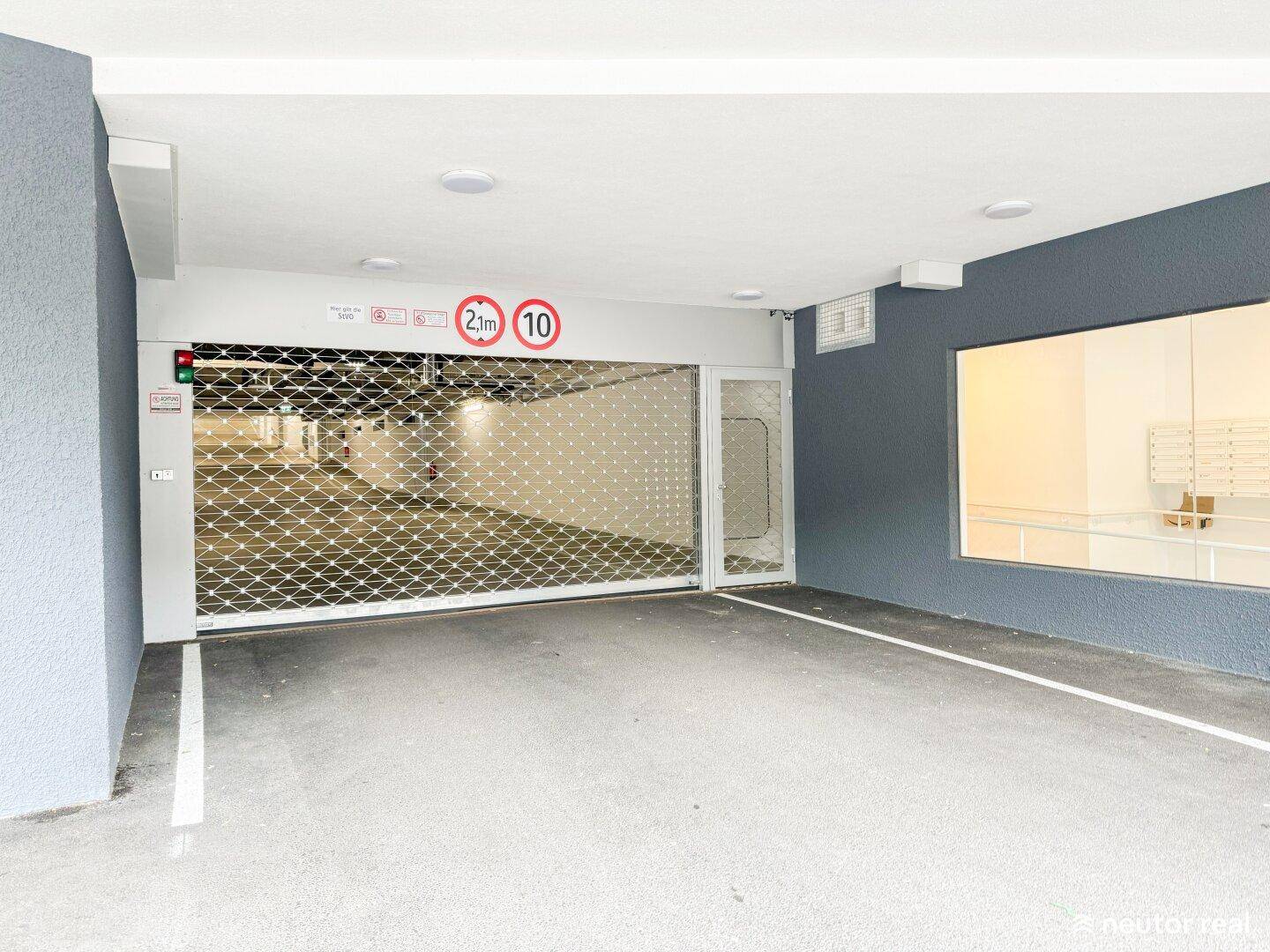 Einfahrt zur Tiefgarage mit geschlossenem Rolltor, Höhenbegrenzung und Geschwindigkeitsanzeige.