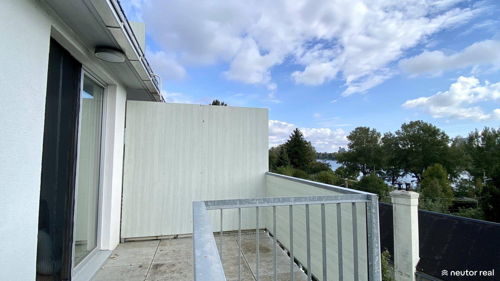 Heller Balkon mit Metallgeländer und seitlichem Blick auf die umliegende Landschaft und den See.