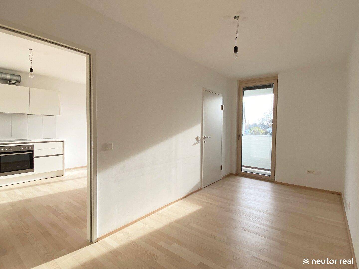 Helles Wohnzimmer mit hellem Parkettboden und Zugang zu einer modernen Küche, lichtdurchflutet.