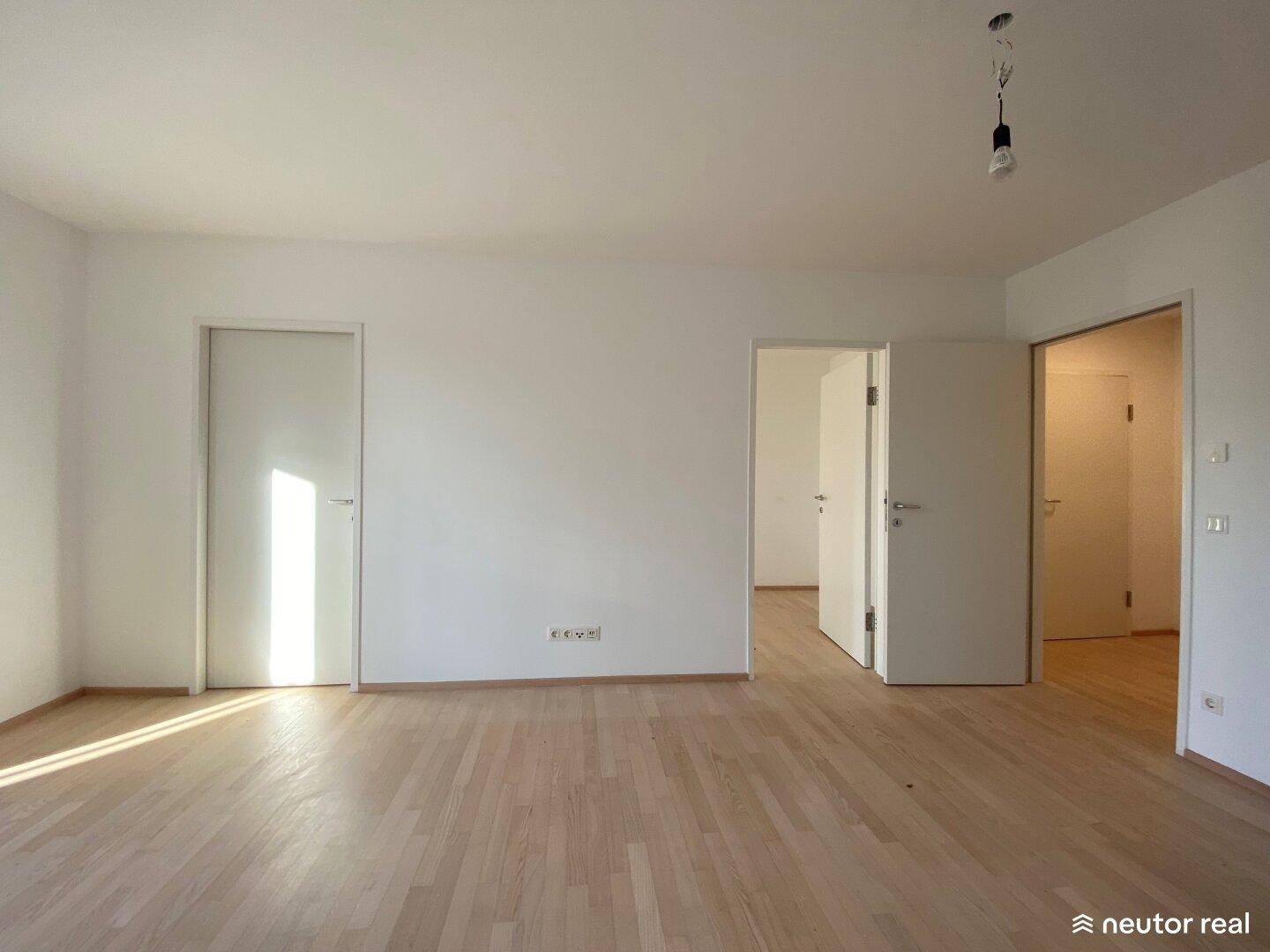 Lichtdurchfluteter Raum mit hellem Parkettboden und mehreren Türen zu angrenzenden Zimmern.