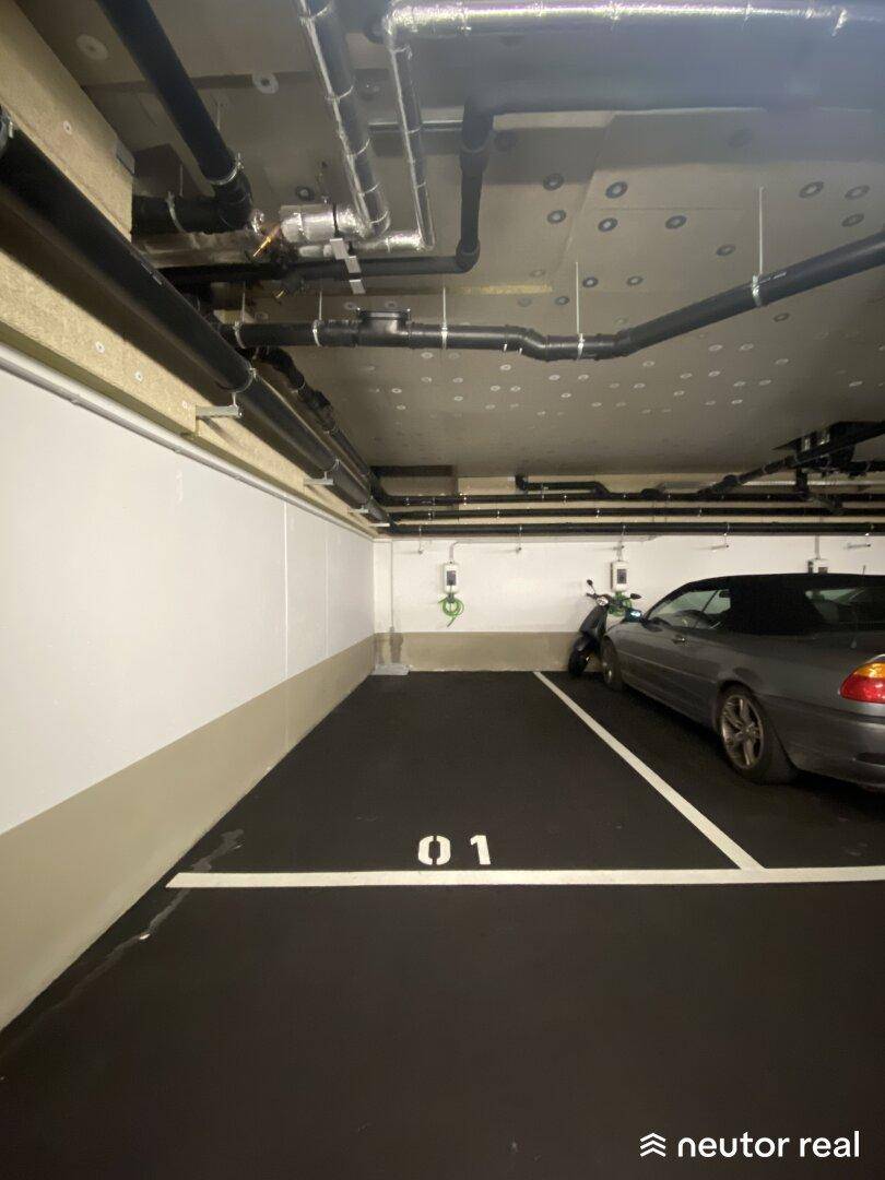 Einzelner Stellplatz in der Tiefgarage mit eigener Ladestation und sichtbaren Rohrleitungen an der Decke.