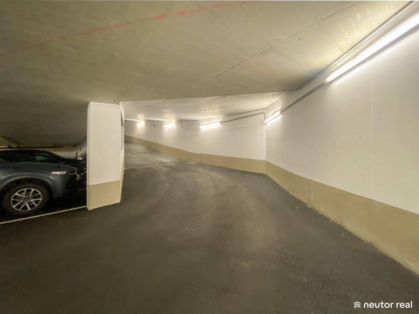 Innenansicht der Zufahrtsrampe in der Tiefgarage, die sich nach unten windet und gut beleuchtet ist.