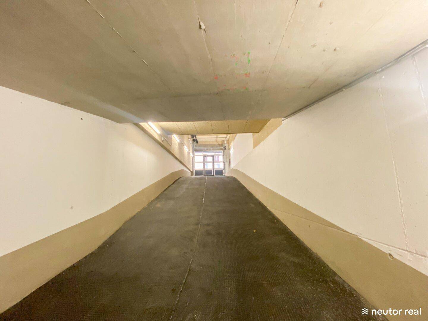 Blick die Rampe hinauf aus der Tiefgarage in Richtung des Ausgangs, gut beleuchtet.