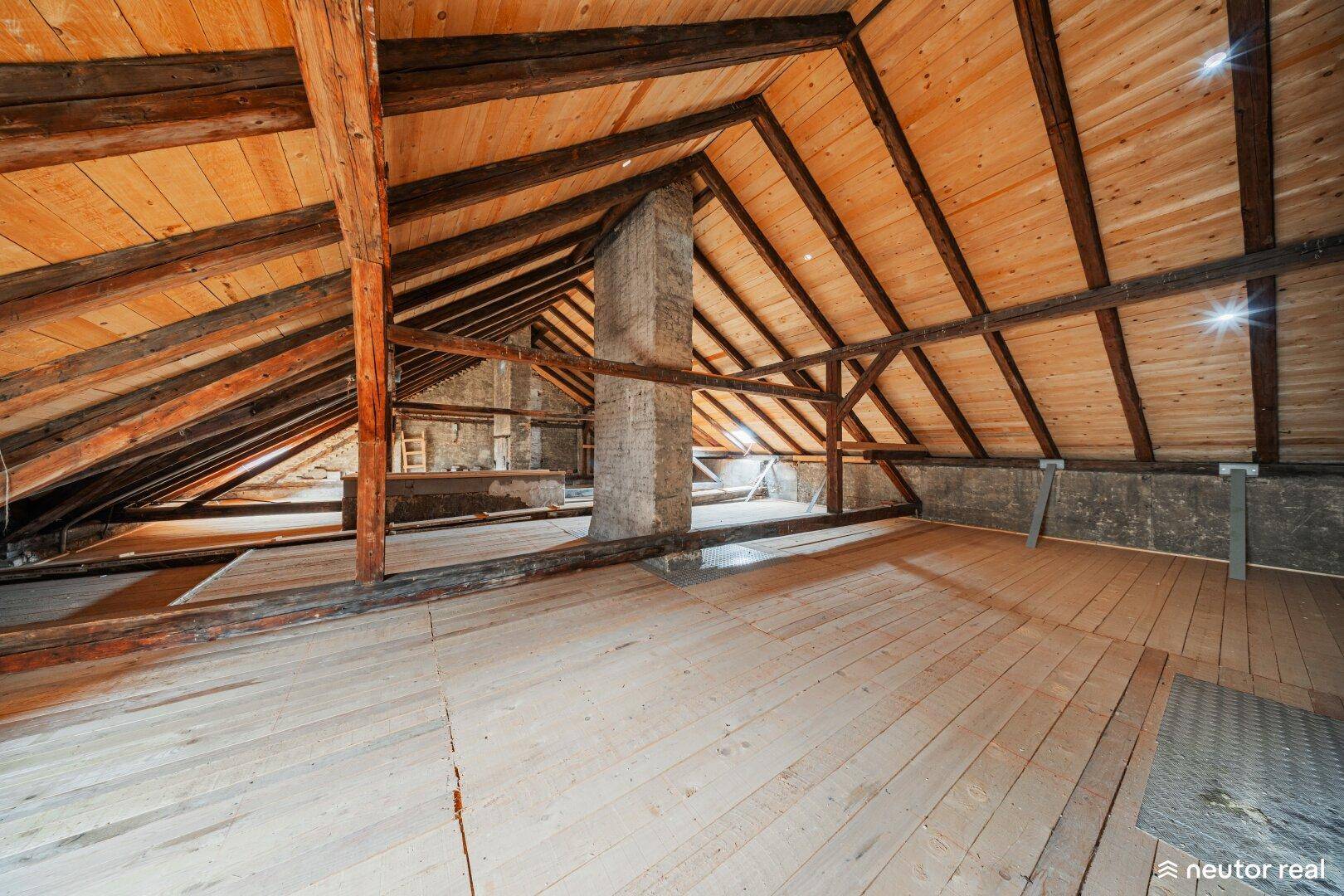 Heller Dachboden mit freiliegenden Holzbalken und schrägen Decken, ideal für zukünftige Nutzung.