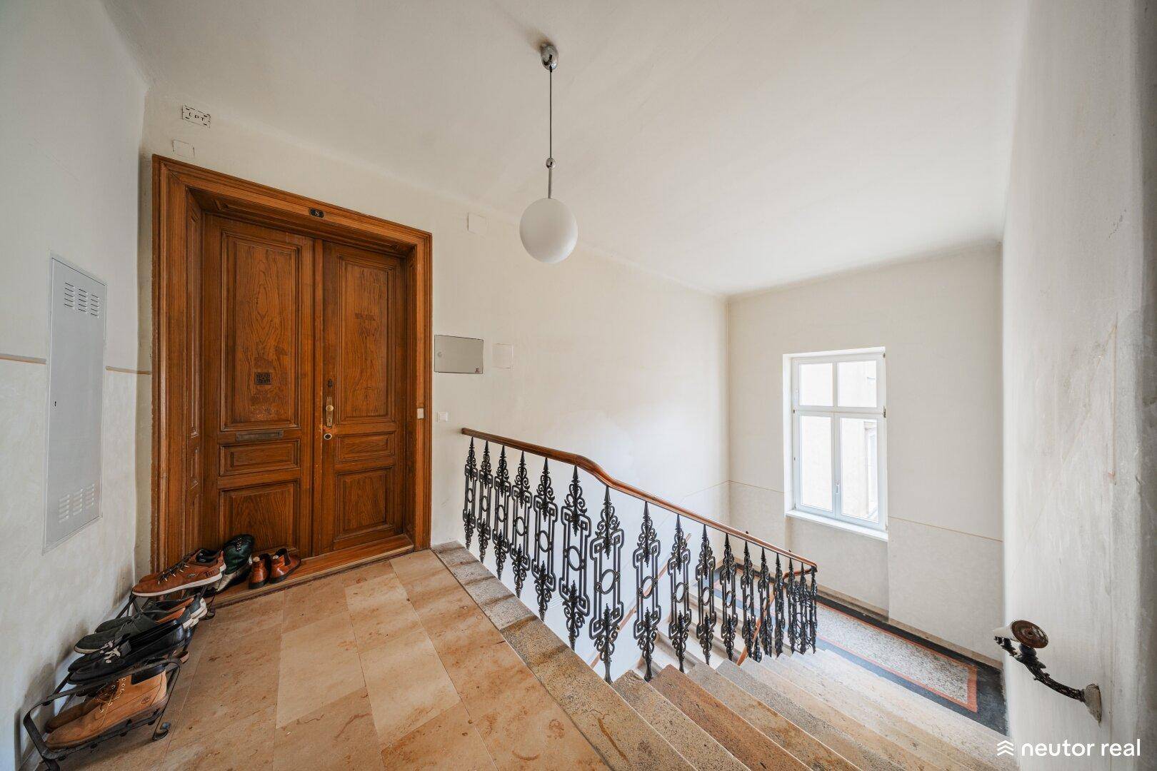 Historisches Treppenhaus mit Marmorboden, schmiedeeisernem Geländer und großer Holztür.