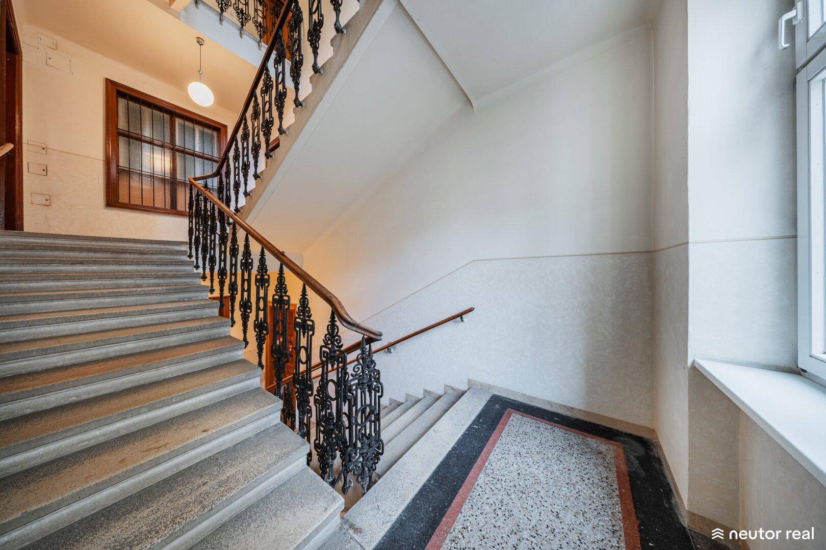 Elegantes Treppenhaus mit Steinstufen, kunstvollem Geländer und dekorativem Terrazzoboden.