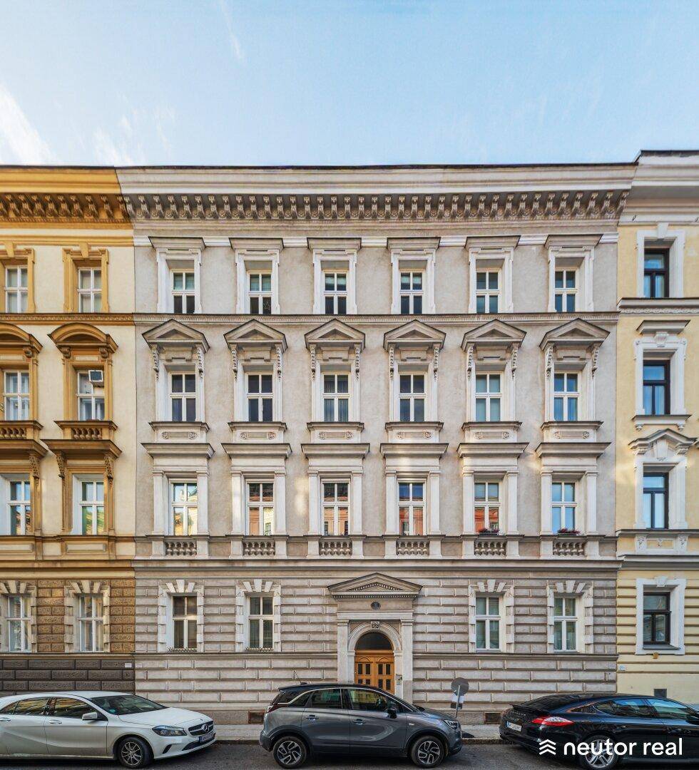 Historische Gebäudefassade mit vielen Fenstern und dekorativen Elementen an einer städtischen Straße.
