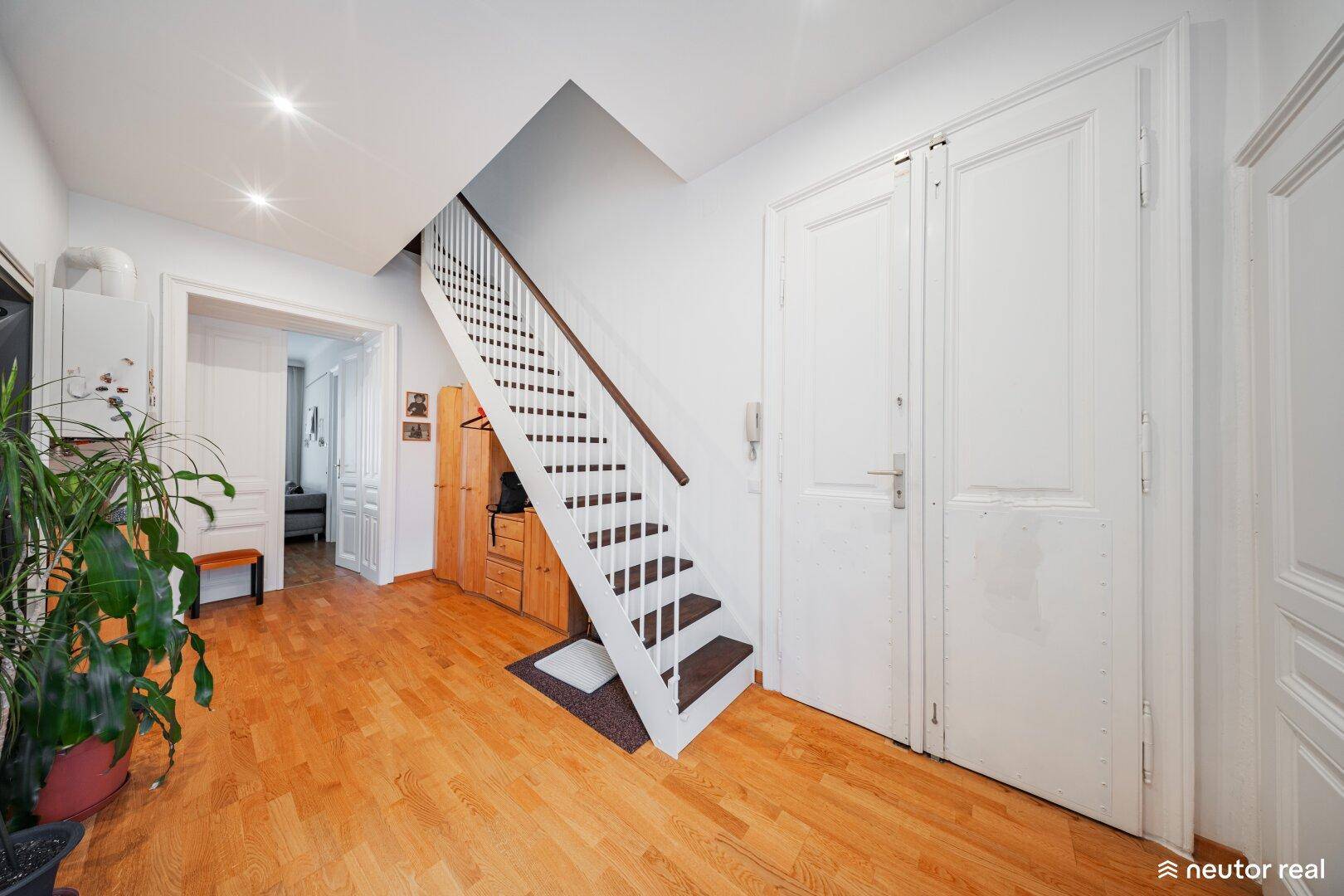 Heller Flur mit Holzparkettboden, weißer Treppe und Zugang zu weiteren Räumen.