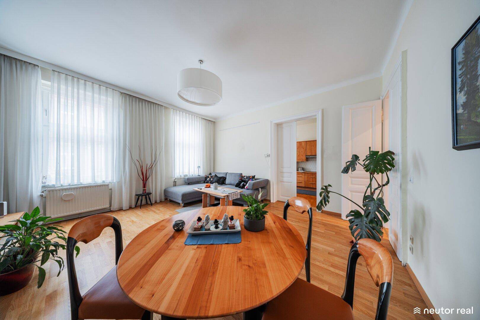 Gemütlicher Wohn-Essbereich mit Holztisch, Sofa und großen Fenstern für viel Tageslicht.